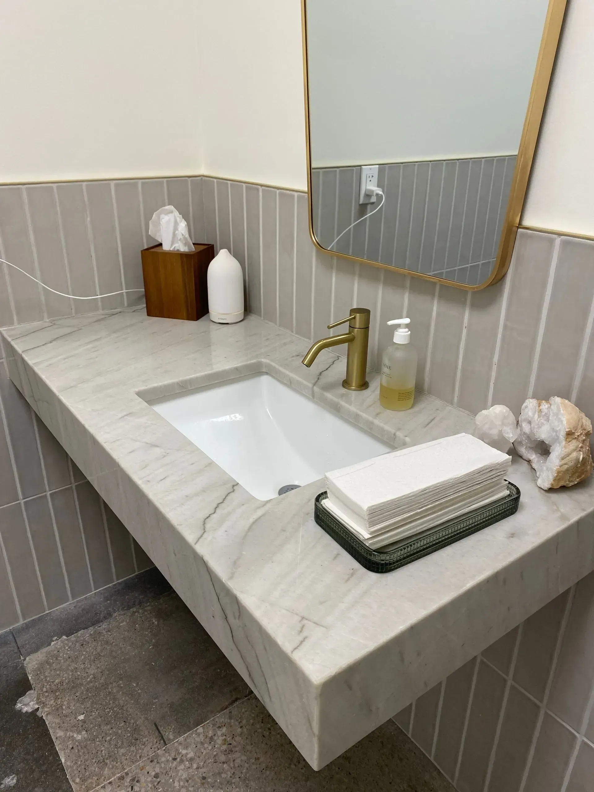 Floating vanity with marble countertop, gold faucet, rectangular sink, and gray tiled wall.