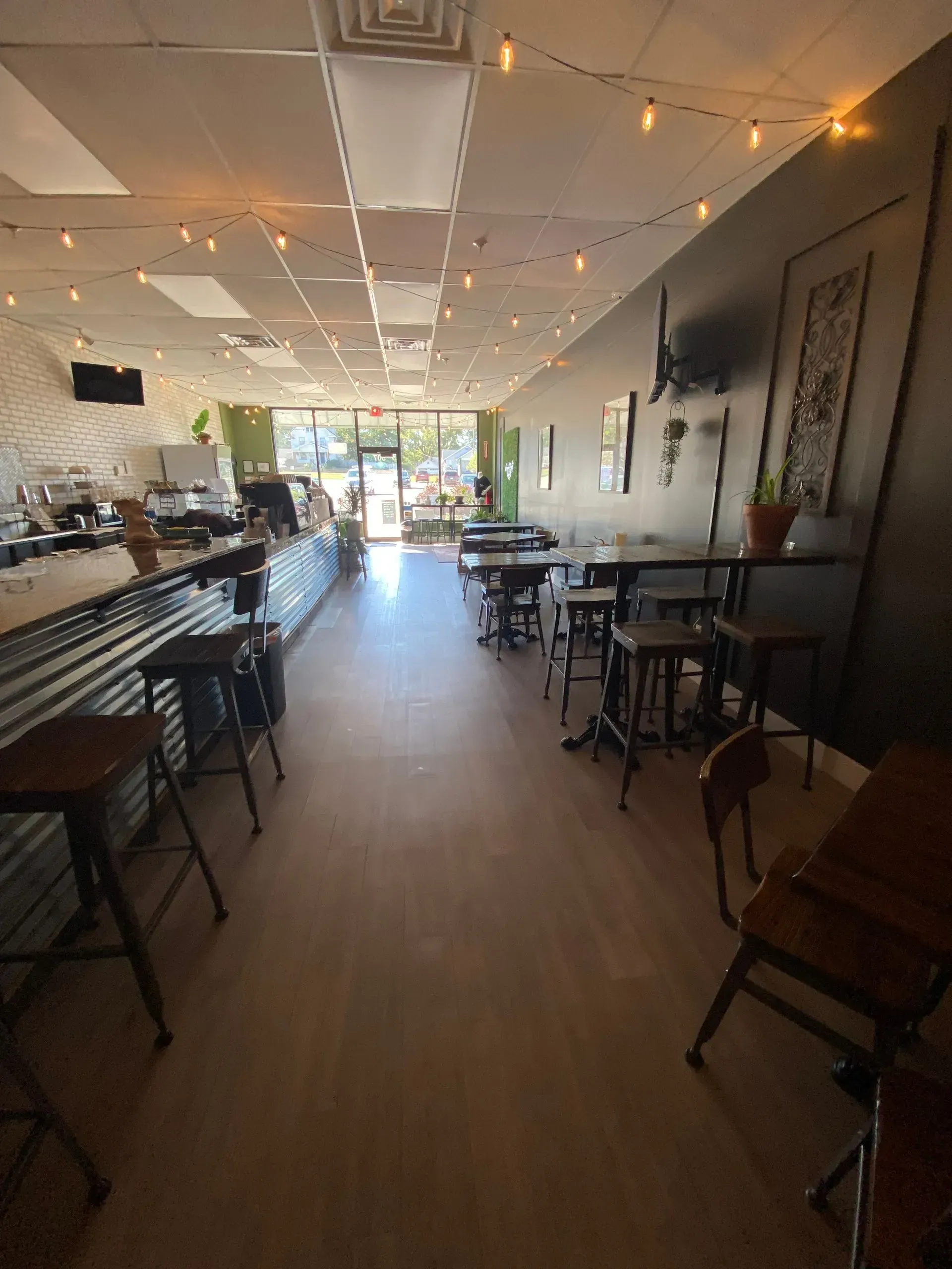 Interior of a cafe with tables and chairs, a counter with stools, and an open doorway.