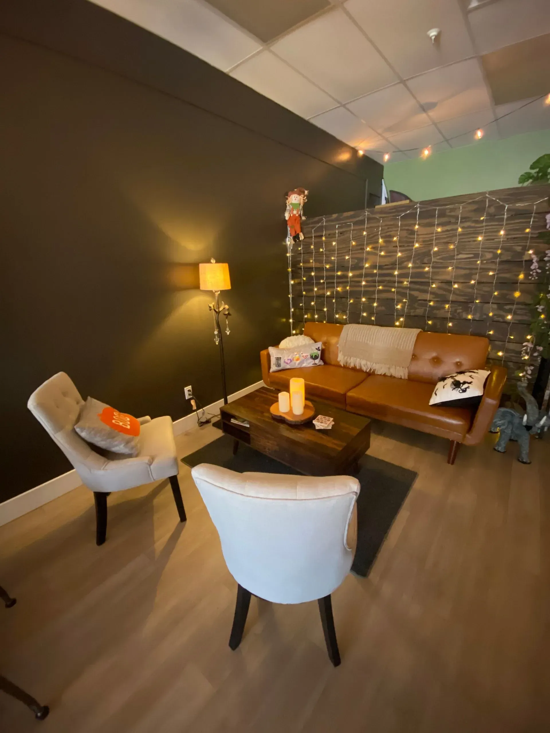 Cozy living room with brown leather couch, two armchairs, wooden coffee table, and string lights.