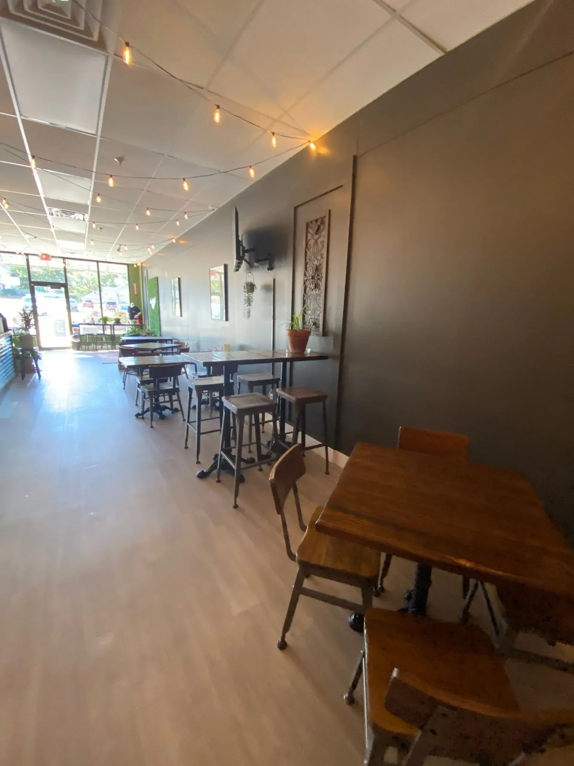 Interior of a cafe with tables, stools, and dark gray walls. String lights hang above.