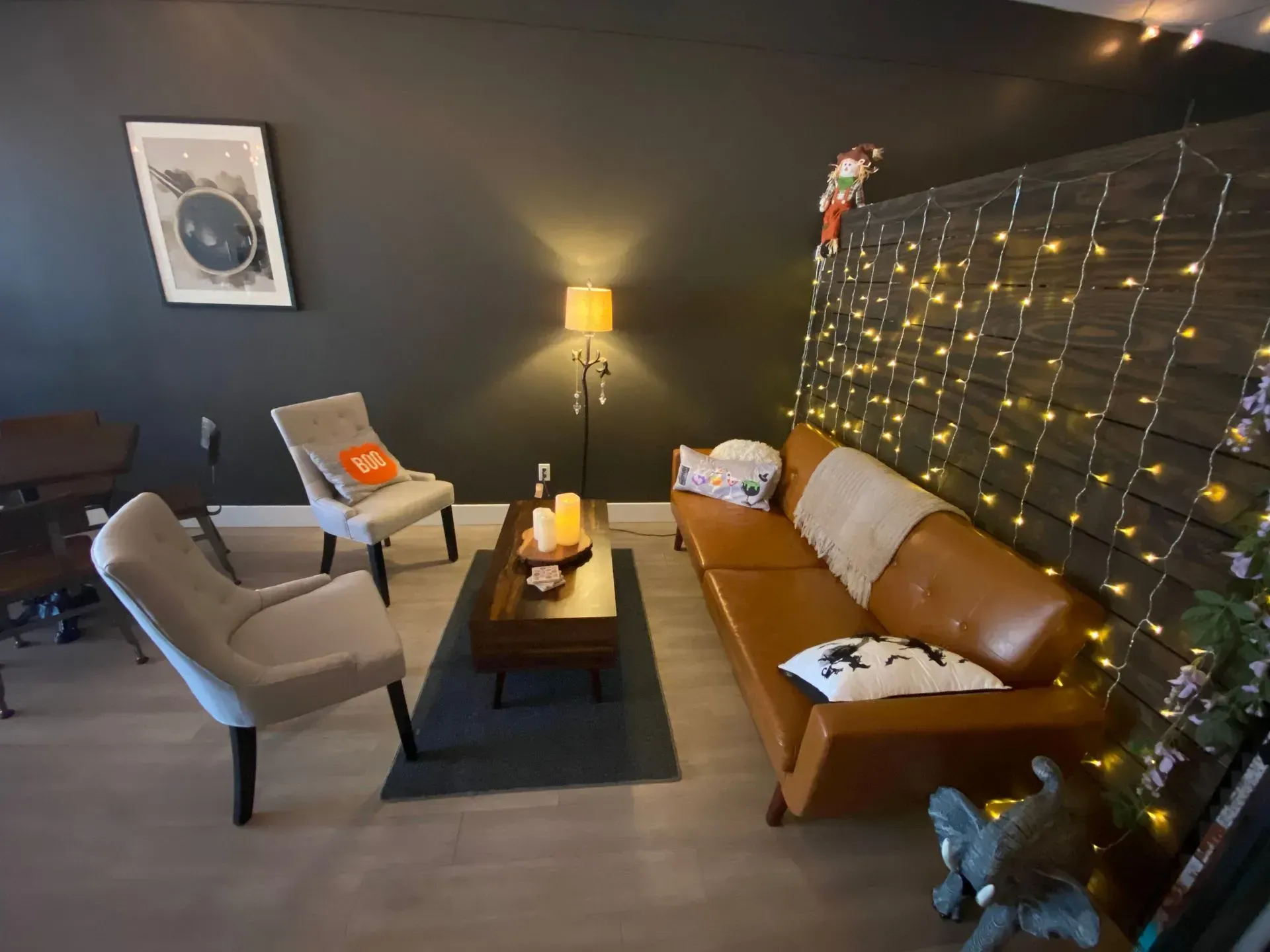 Living room with leather sofa, chairs, coffee table, and string lights on a dark wall.