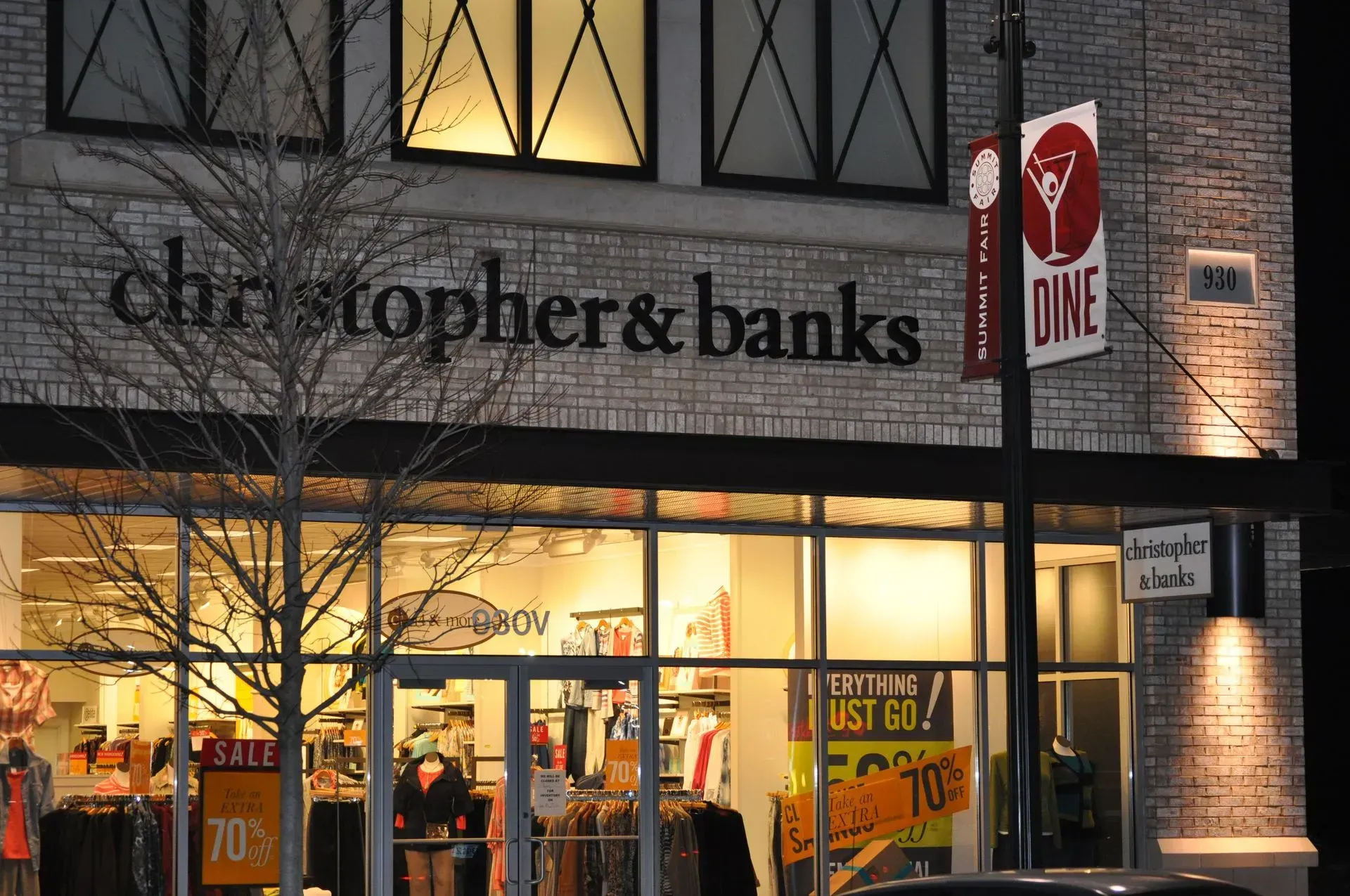 Christopher & Banks store at night, with illuminated sign and storefront display, brick building.