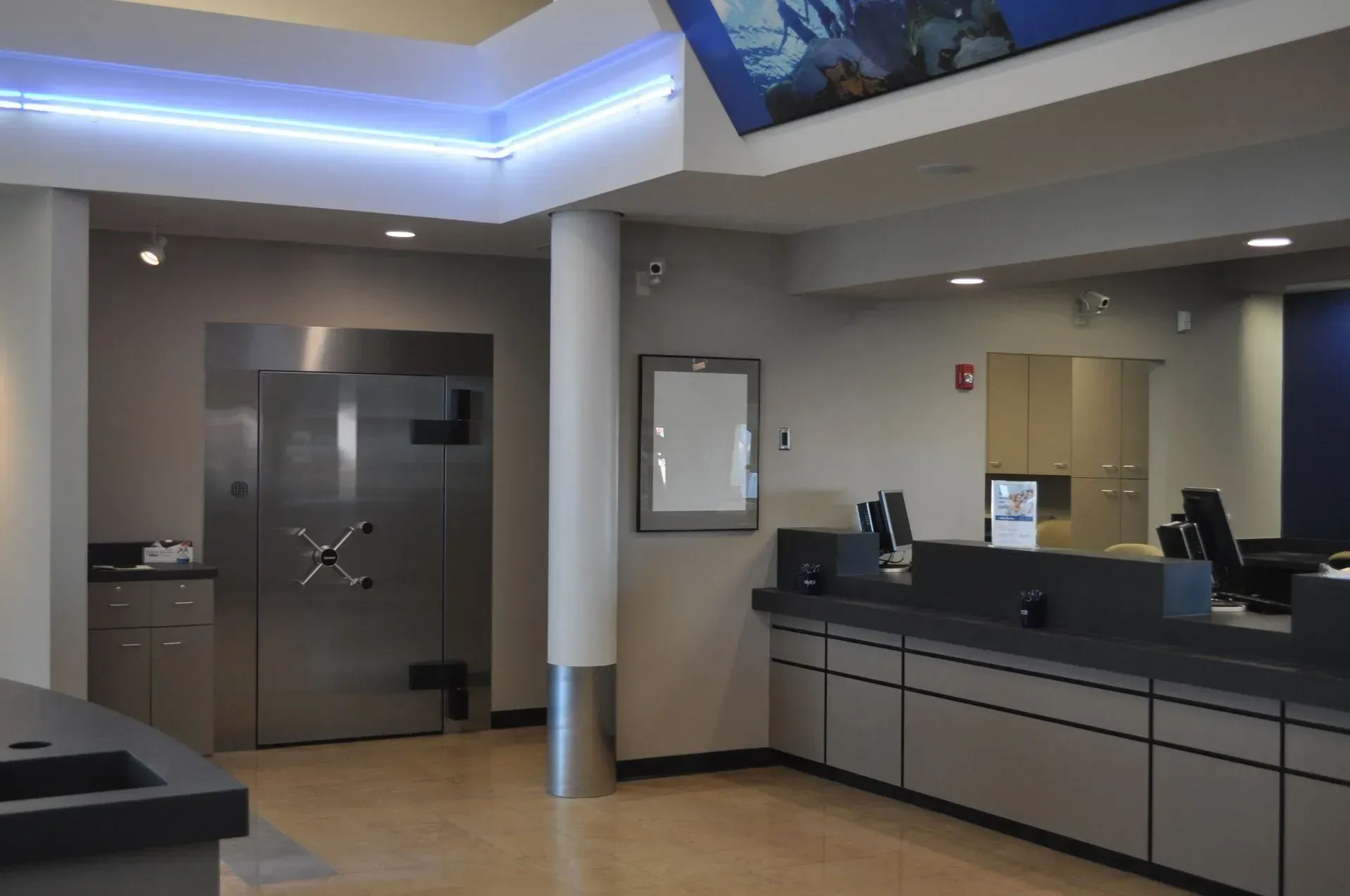 Interior of a bank with a large metal vault door, teller counters, and blue accents.