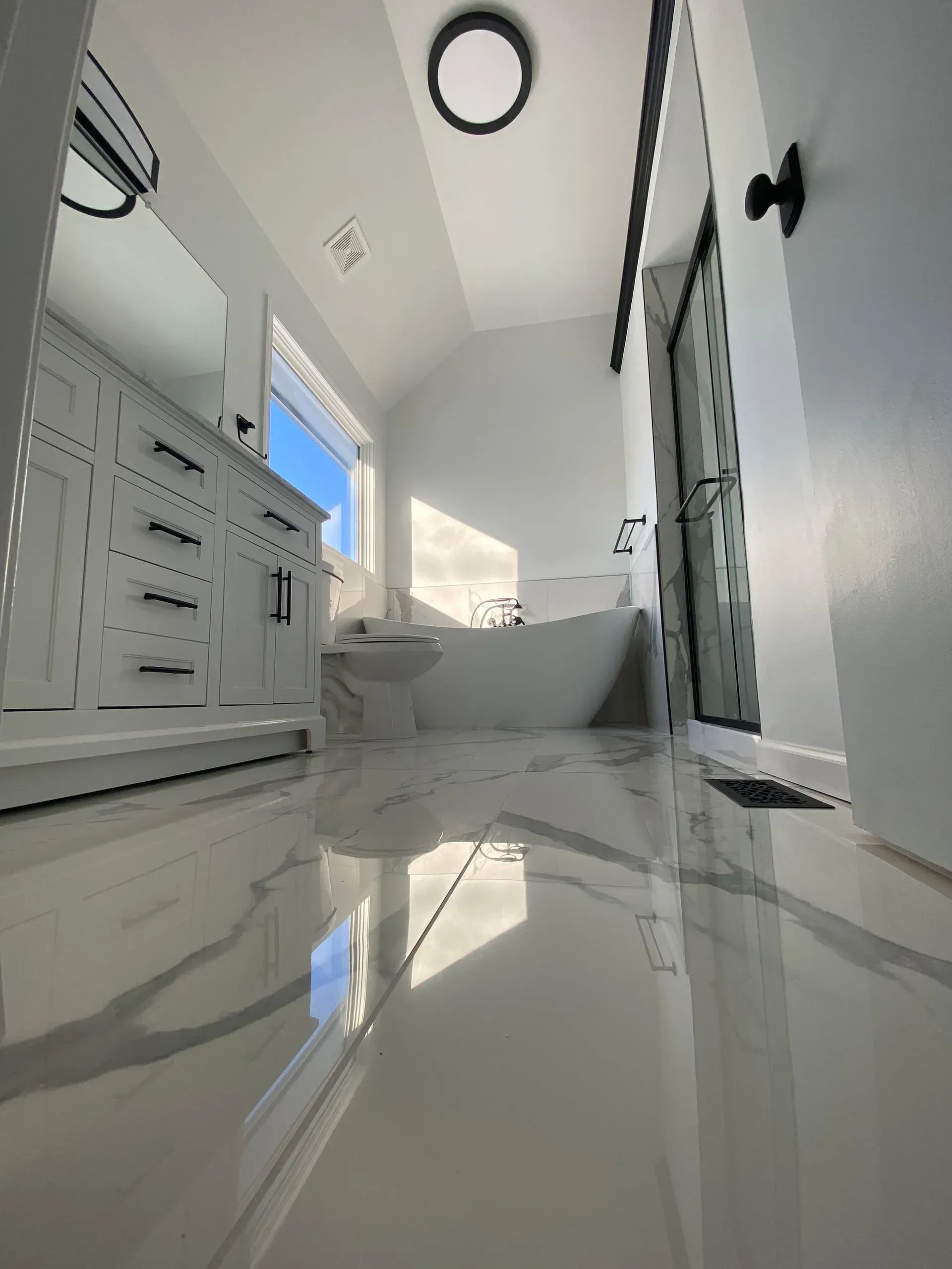 Bright, modern bathroom with white marble floors, a white vanity, and a freestanding tub.