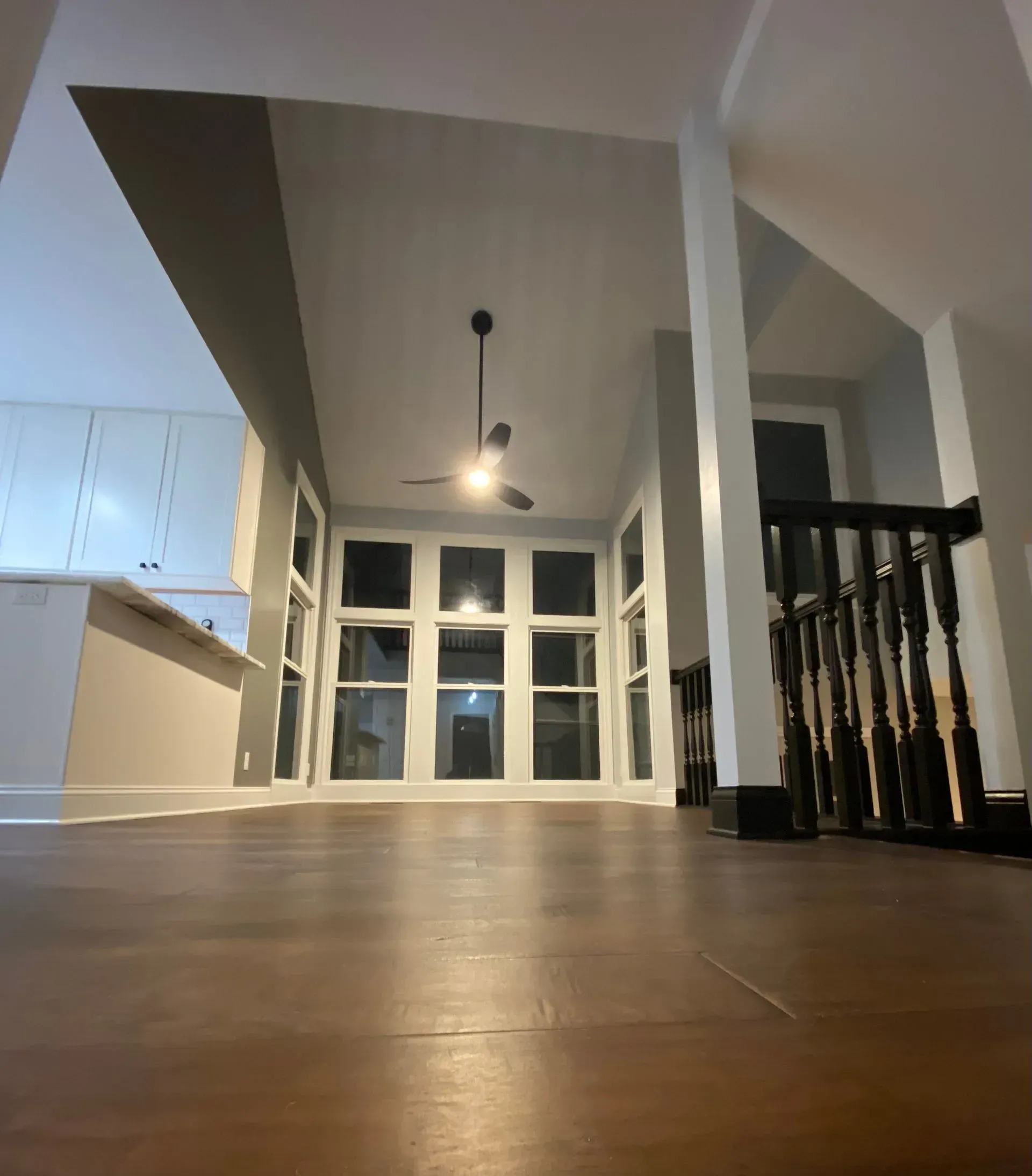 Low-angle view of a room with hardwood floors, many windows, and a staircase with a black banister.