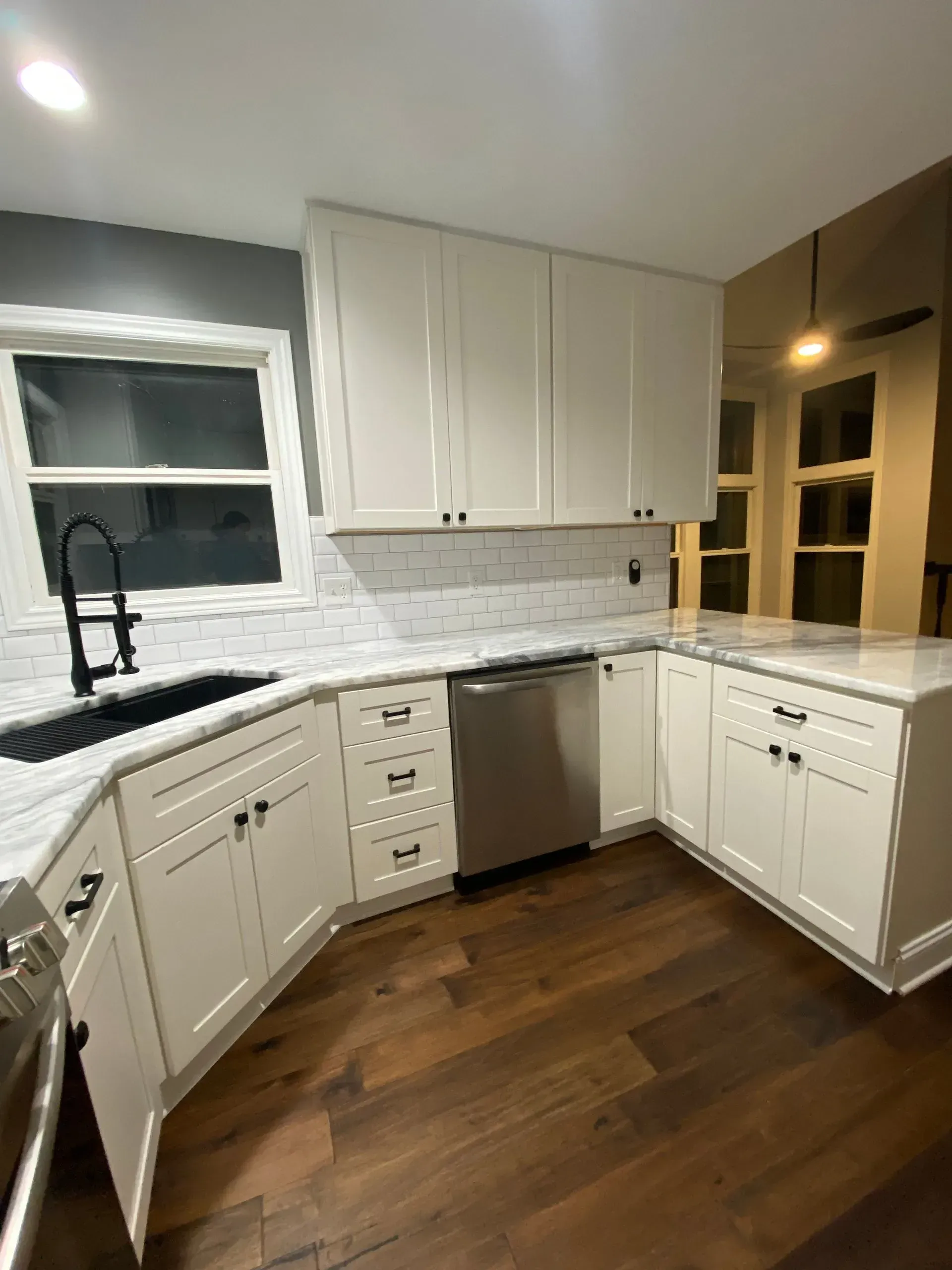 White kitchen with dark wood floors, white cabinets, marble backsplash and countertops, stainless steel appliances.
