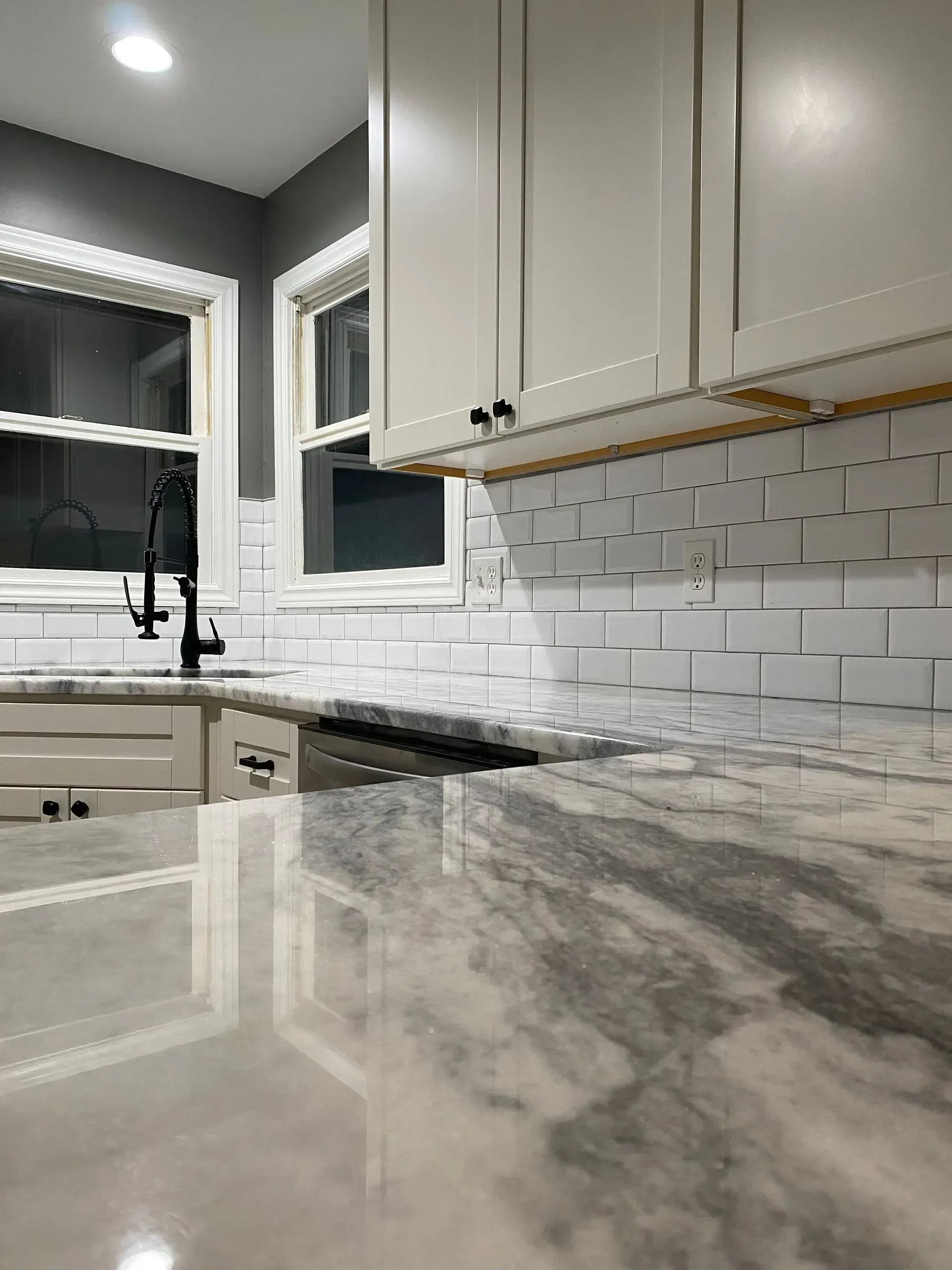 Kitchen with white cabinets, marble countertop, subway tile backsplash, and black faucet.