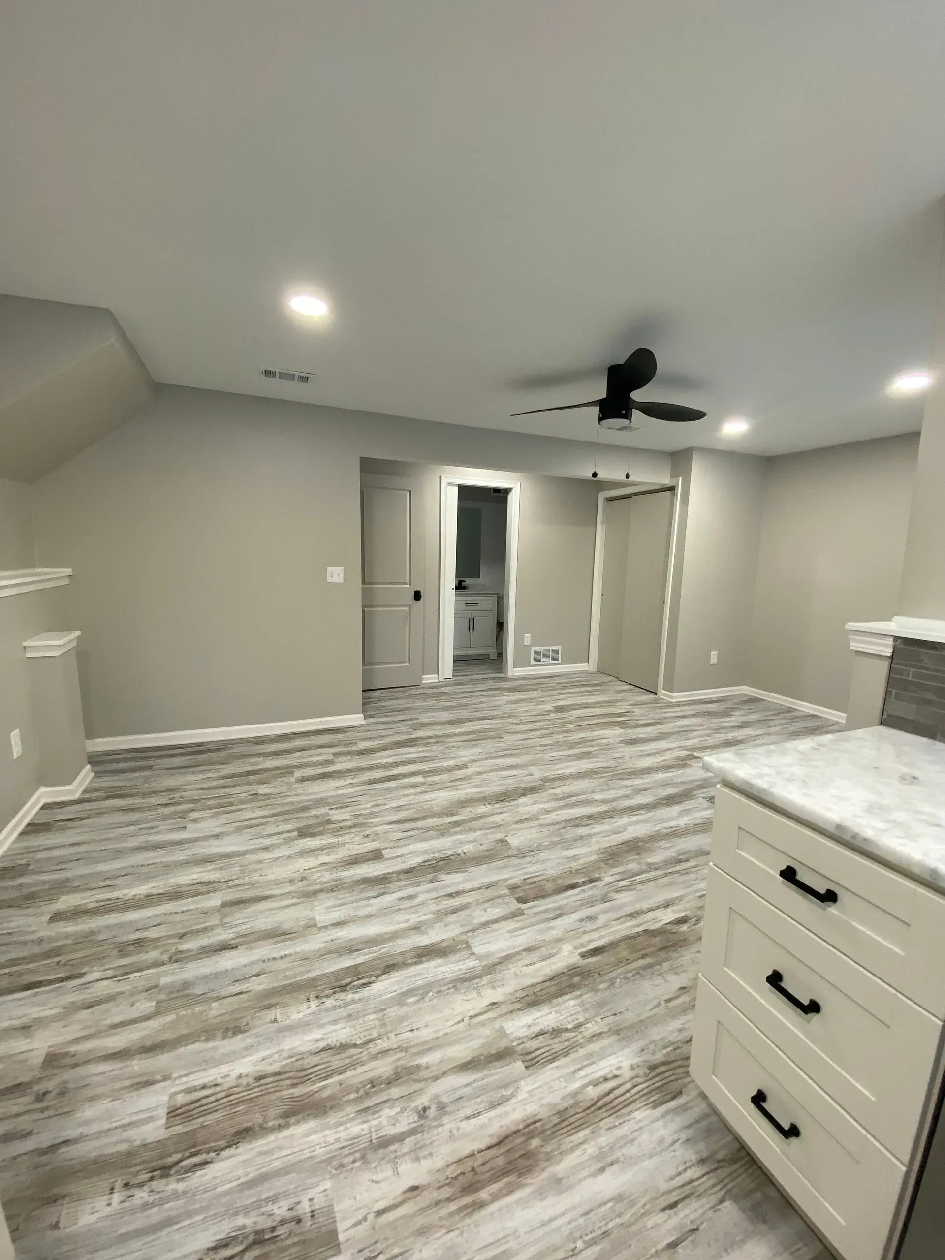 A room with gray walls, wood-look flooring, and a ceiling fan, with a white cabinet in the foreground.
