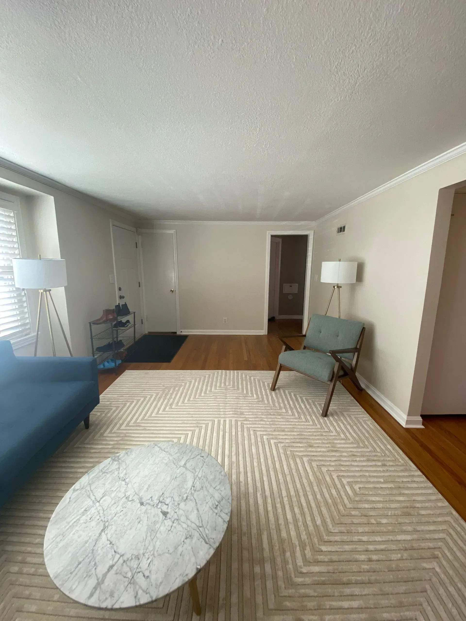 Living room with blue sofa, patterned rug, light colored walls, chair, and coffee table.