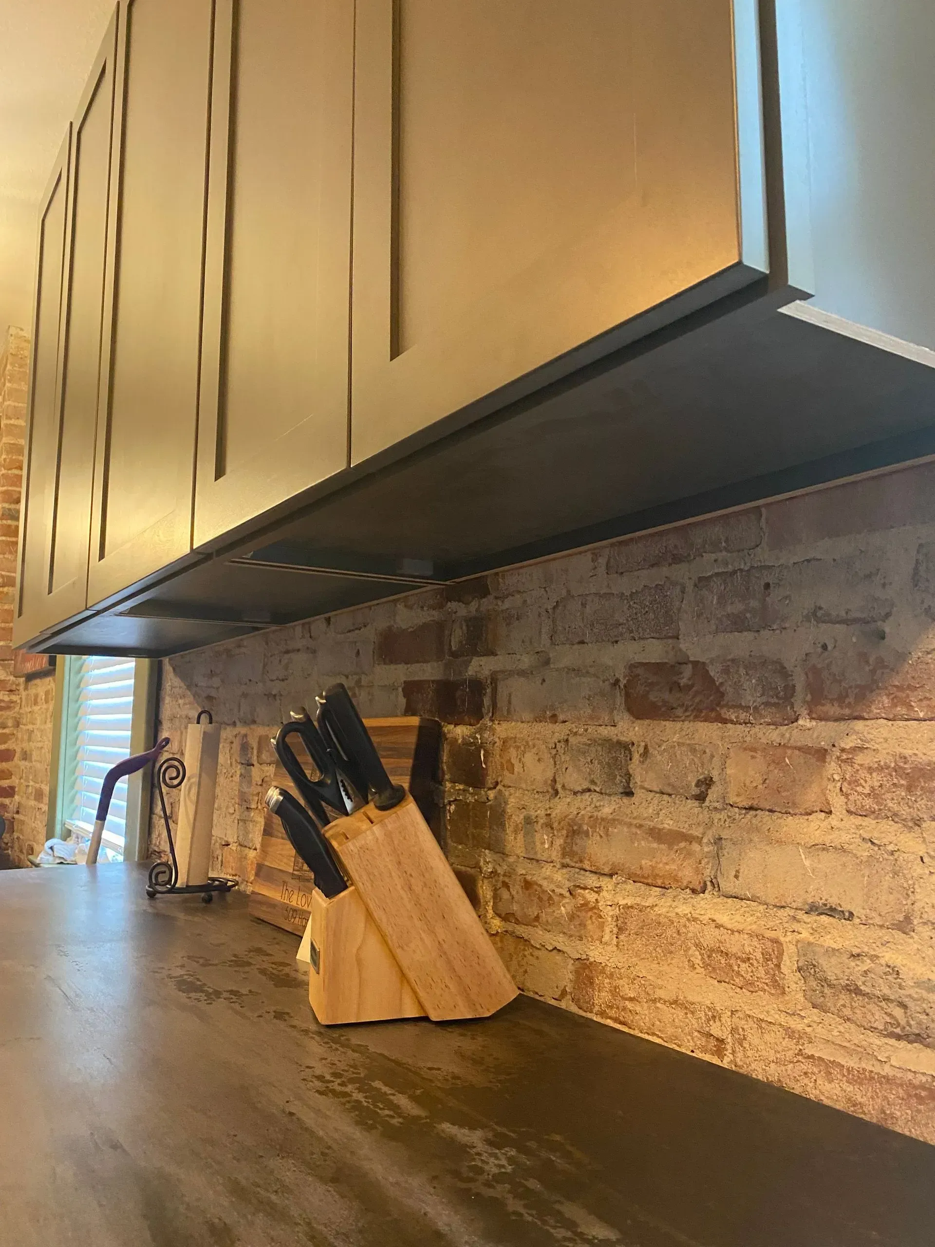 Kitchen with brick backsplash, dark cabinets, and knife block on the counter.