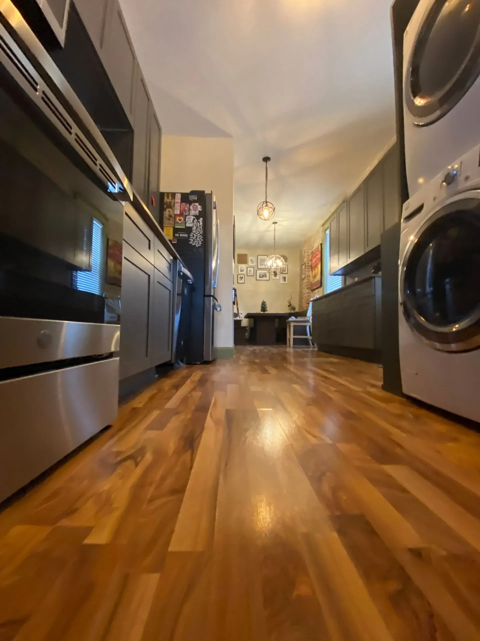 Long, narrow kitchen with wood floors, dark gray cabinets, and a washing machine.
