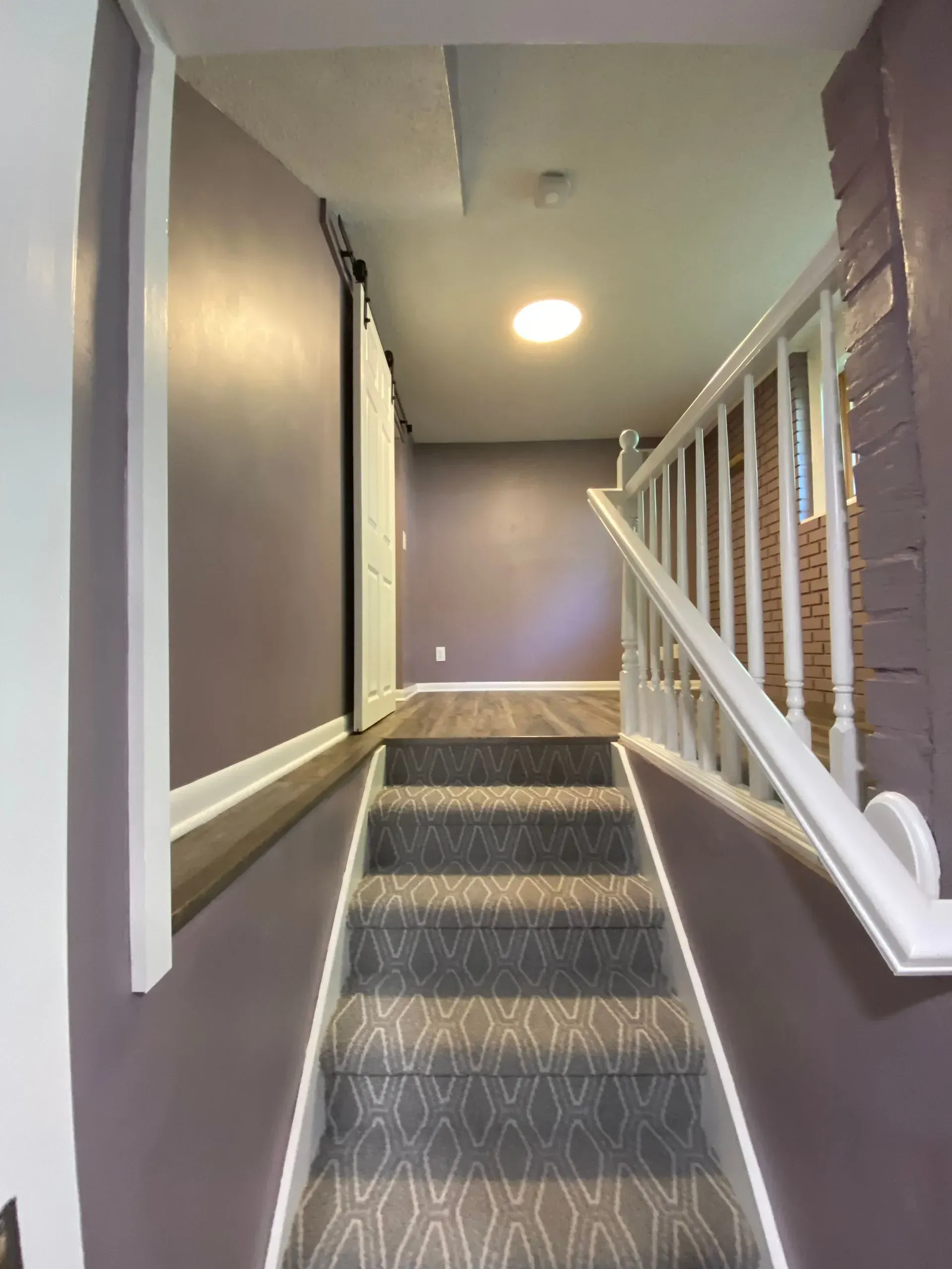 Staircase leading up to a hallway. Gray carpet on steps, purple walls. White handrail on right.