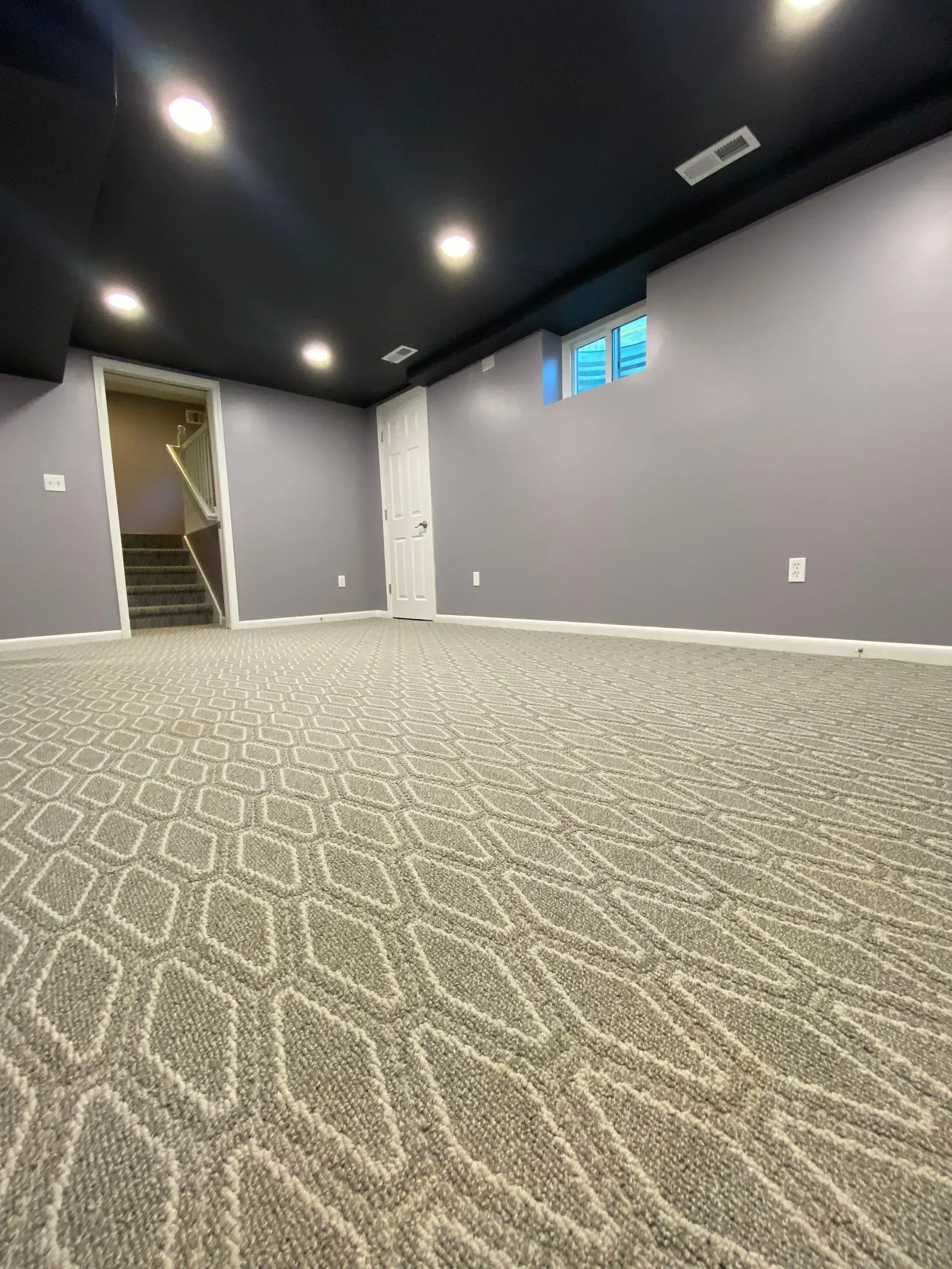 Gray carpeted basement with gray walls, a black ceiling, and recessed lighting. A door and stairs are visible.