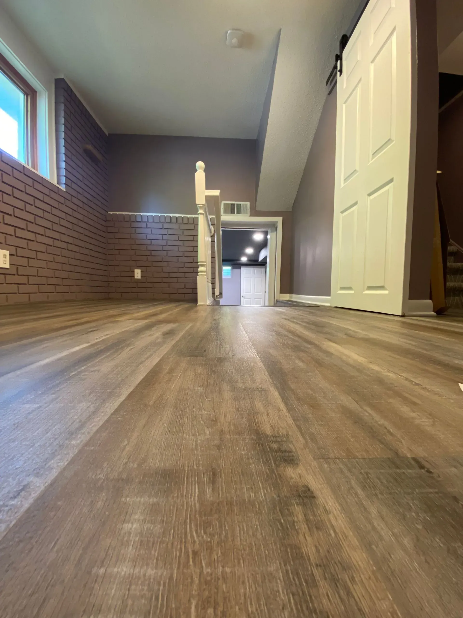 Newly installed wood-look flooring in a long room with brick wall, door, and a window.