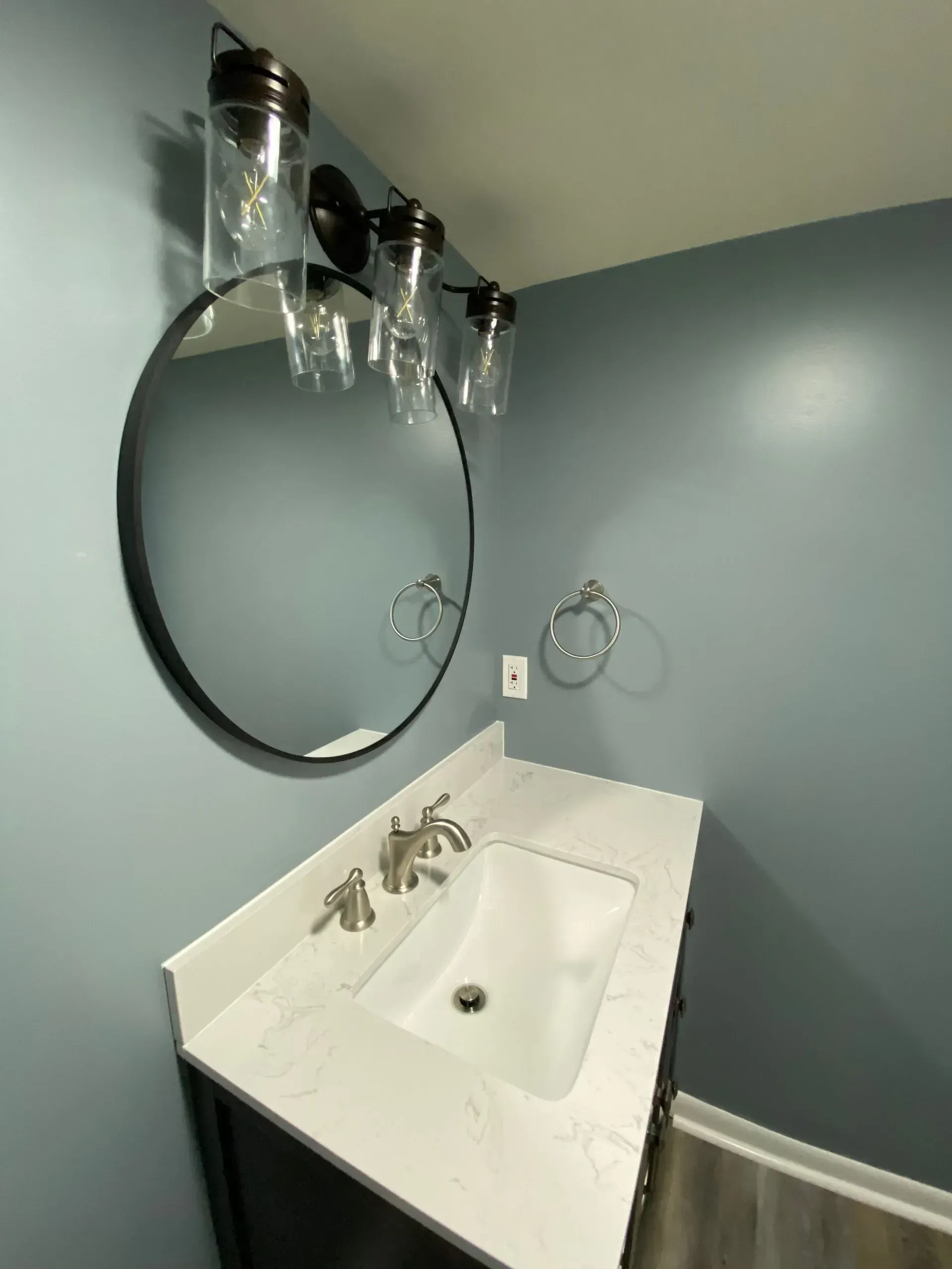 Bathroom with a blue wall, round mirror, vanity, and light fixture.