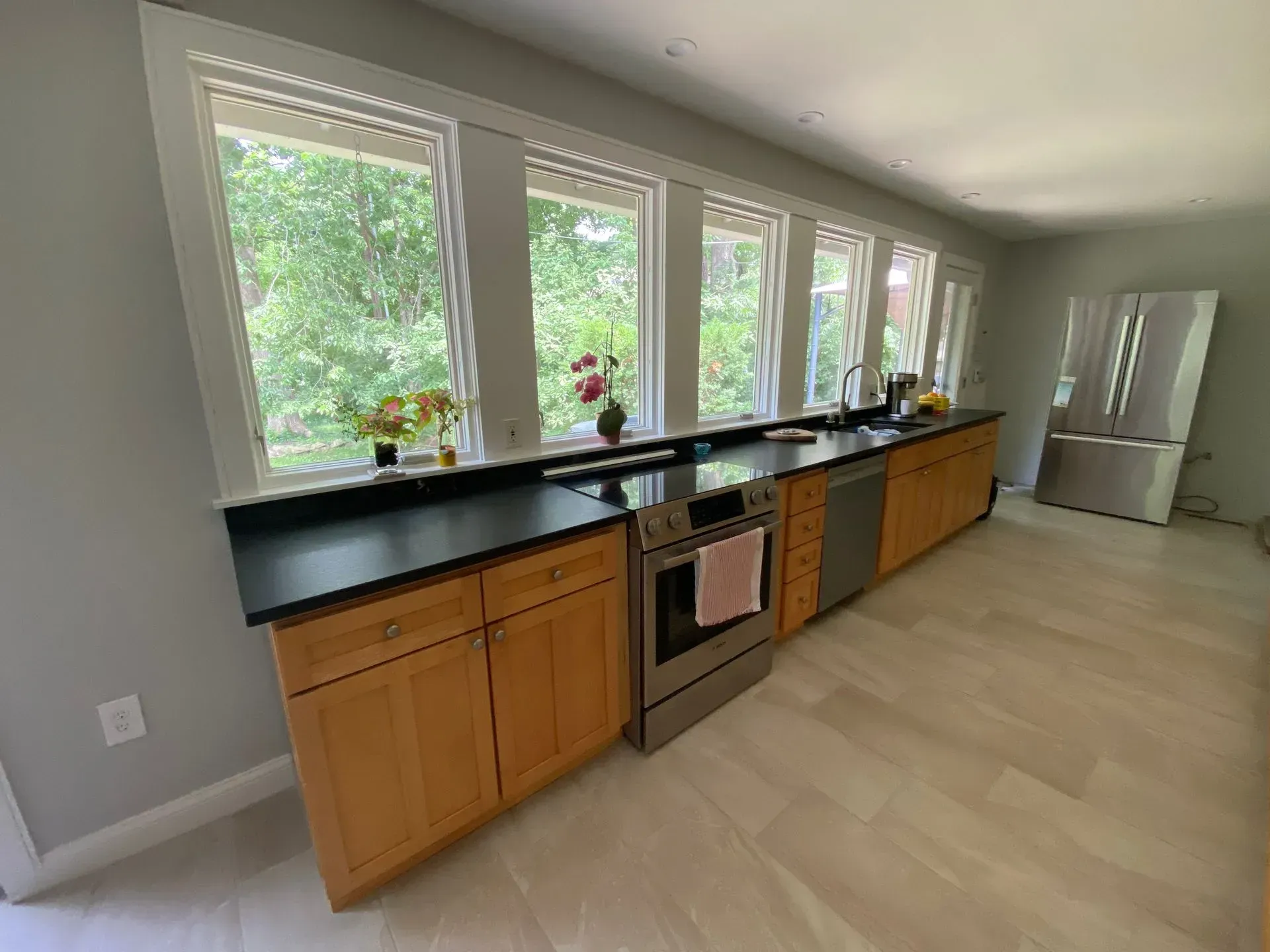 Kitchen with wood cabinets, dark countertop, stainless steel appliances, and large windows.