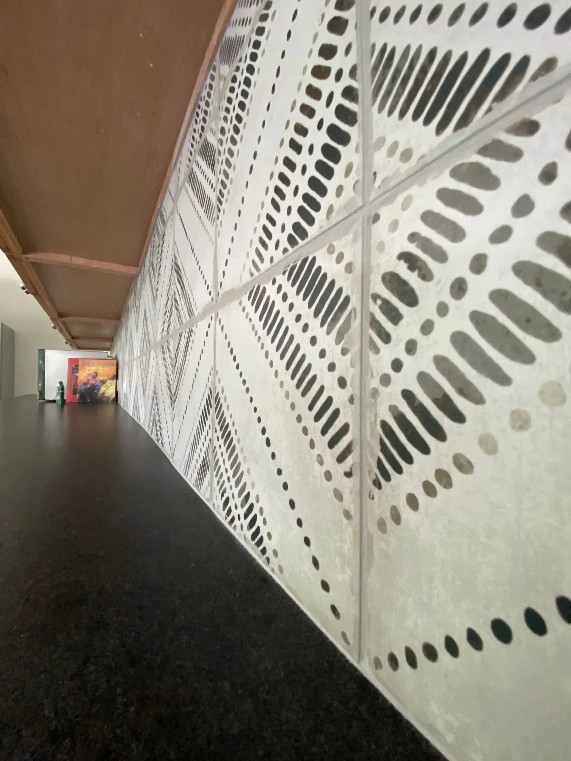 Long hallway with a patterned white wall. A black surface and brown ceiling are visible.