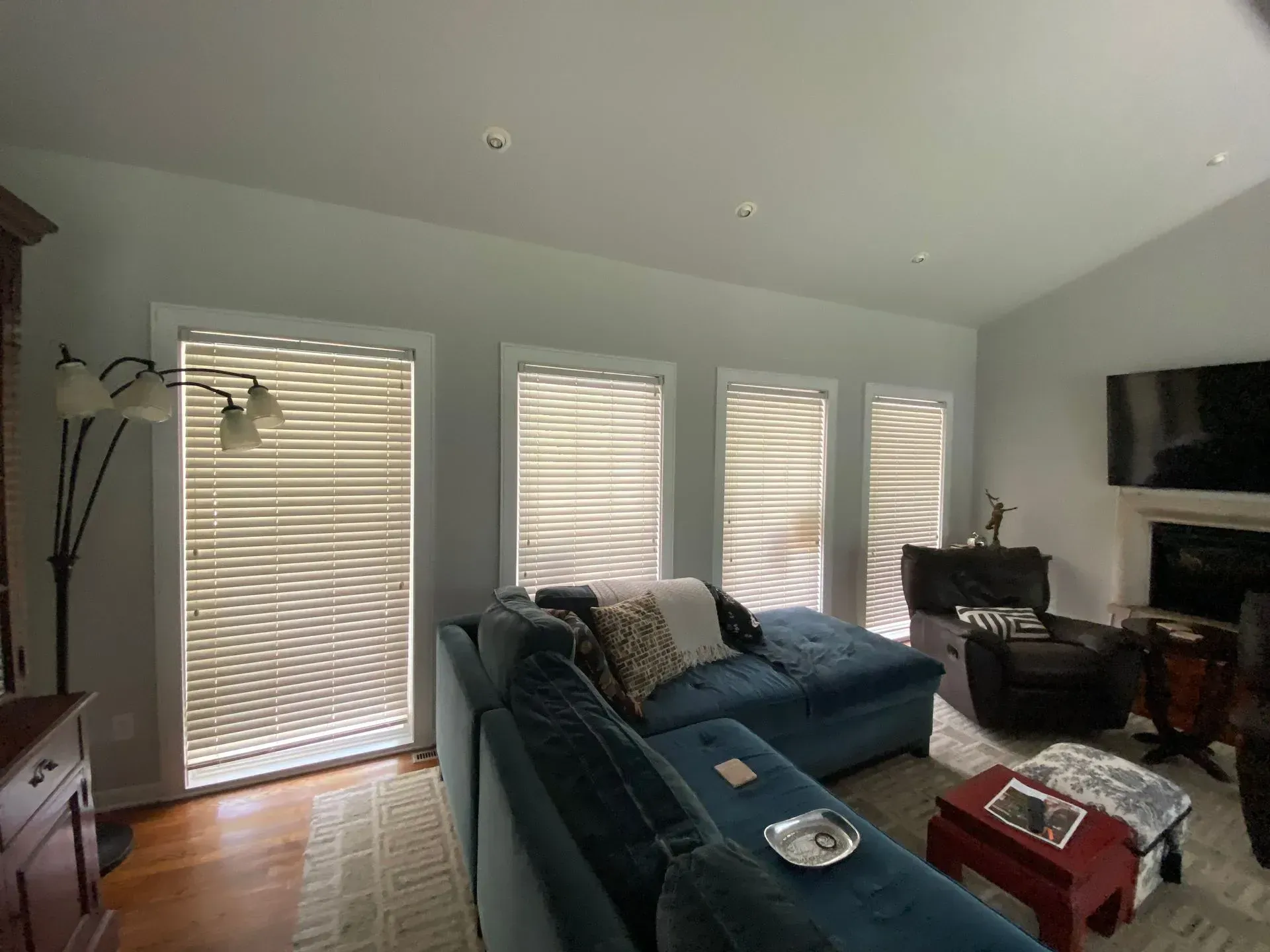 Living room with blue sectional, three windows with blinds, and a fireplace.