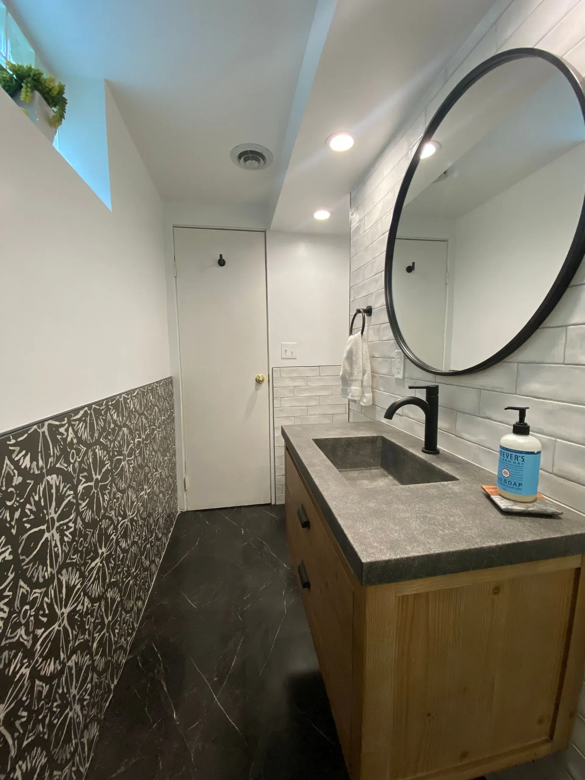 Bathroom with black and white patterned tile, a wooden vanity, and a round mirror.