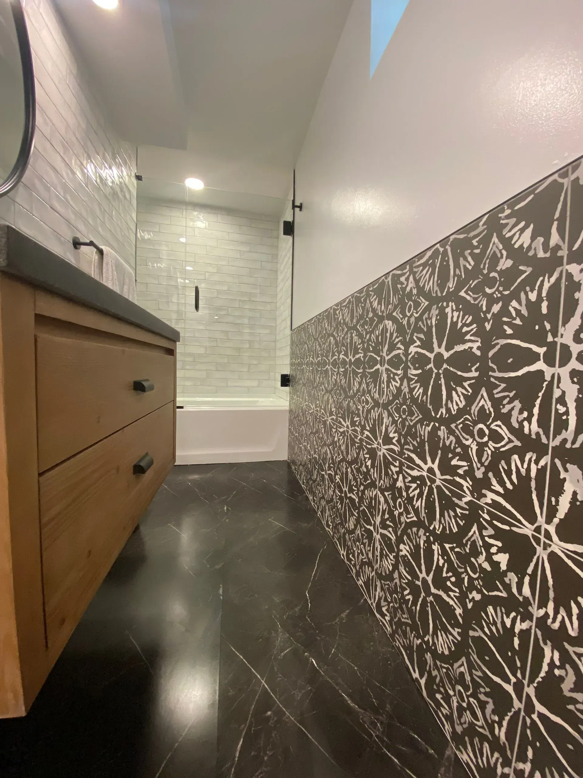 Bathroom with dark floor, wood vanity, patterned wall, and tiled shower.