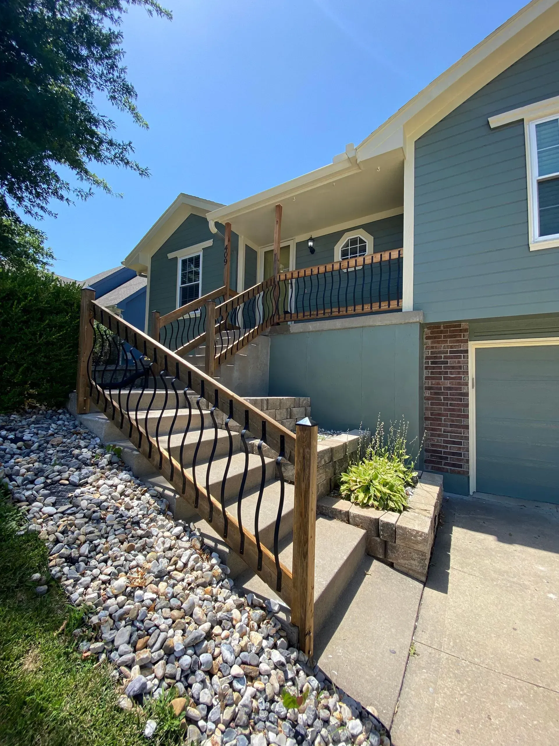 A two-story blue house with a front porch and steps leading up from a rock-covered landscape.