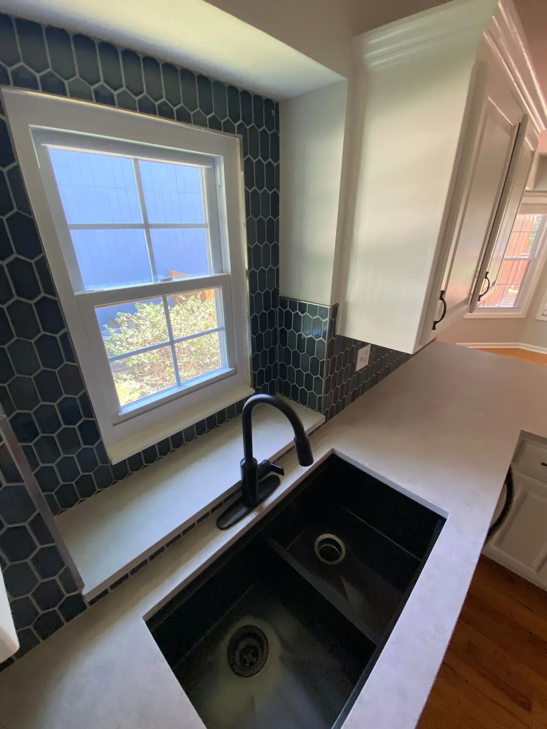 Black kitchen sink with black faucet, below a window with blue-tiled backsplash.