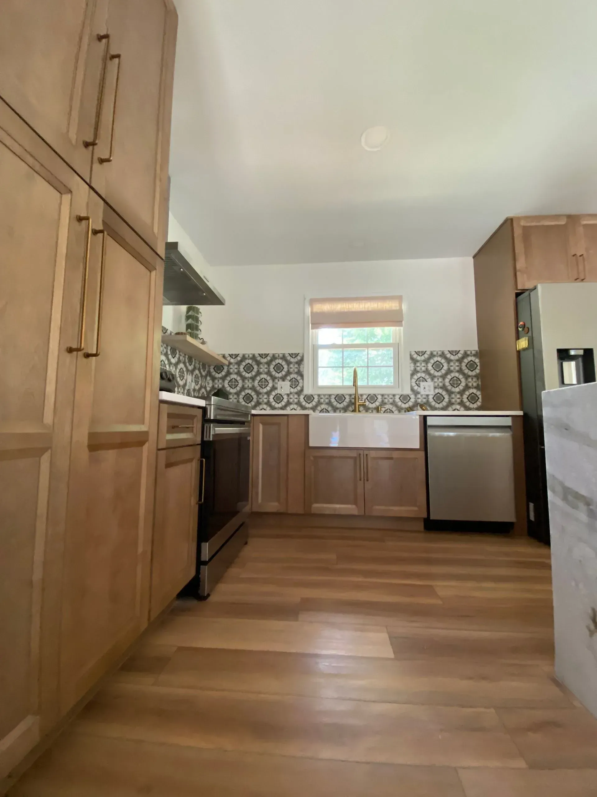 Kitchen with light wood cabinets, patterned backsplash, stainless steel appliances, and wood floors.