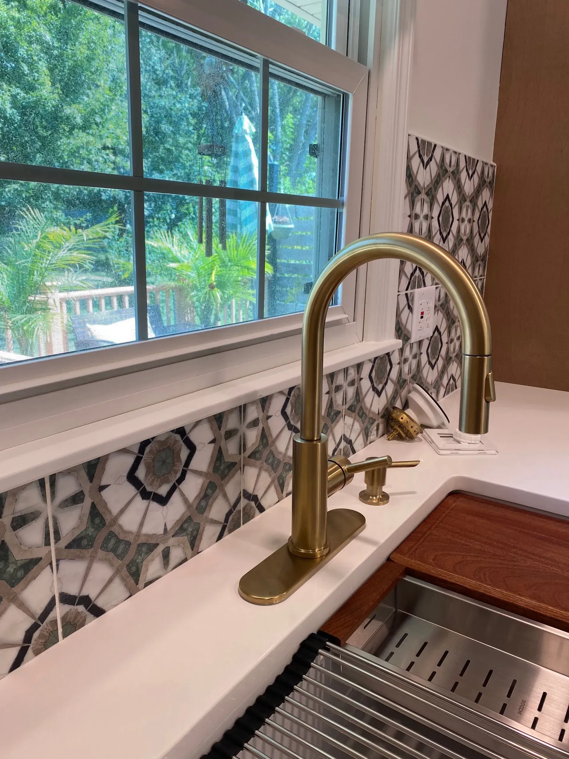 Gold faucet over a white kitchen sink, set against decorative tile backsplash and a window view.