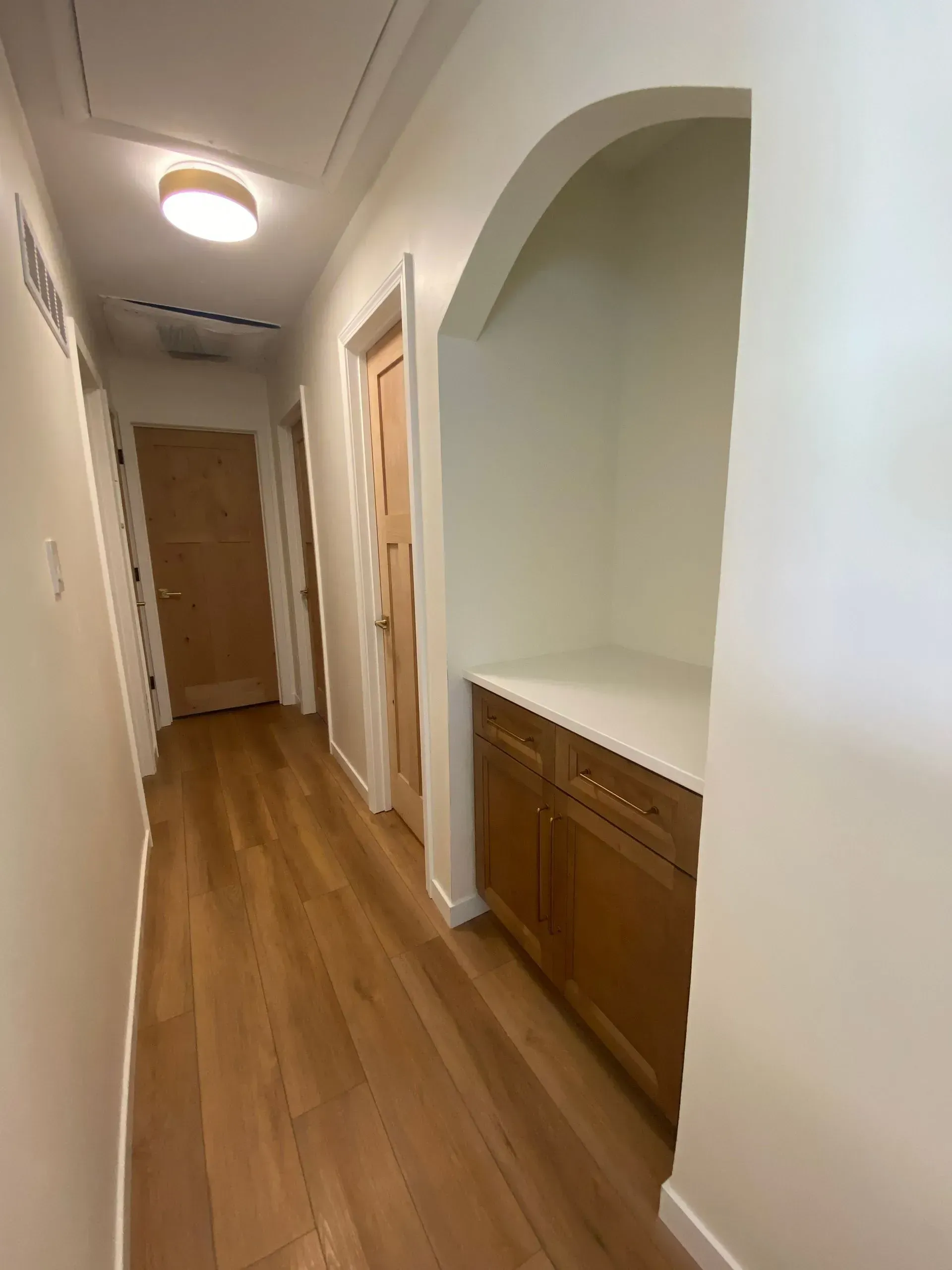 Hallway with wood floors, doors, and built-in cabinet. Archway leads to a recessed area.
