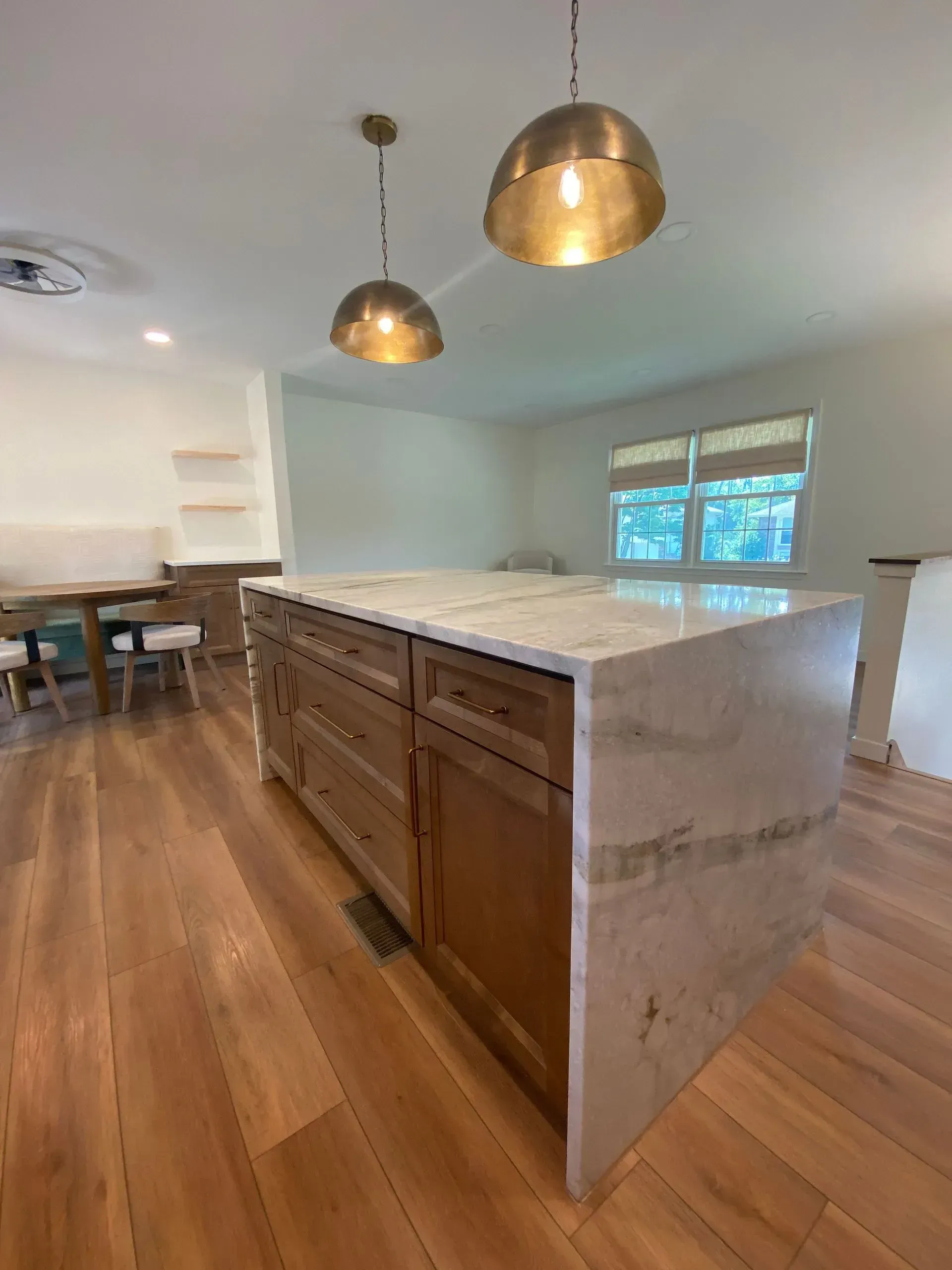 Kitchen with wood cabinets, stone island countertop, gold pendant lights, and hardwood floors.
