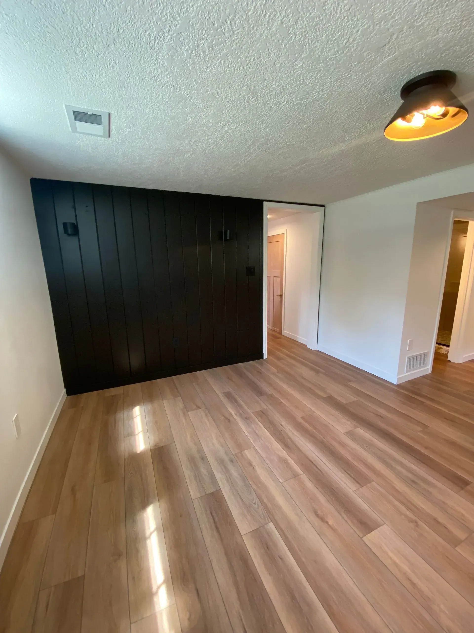Empty room with wood floors and a dark paneled wall. A sliding door leads to another room.