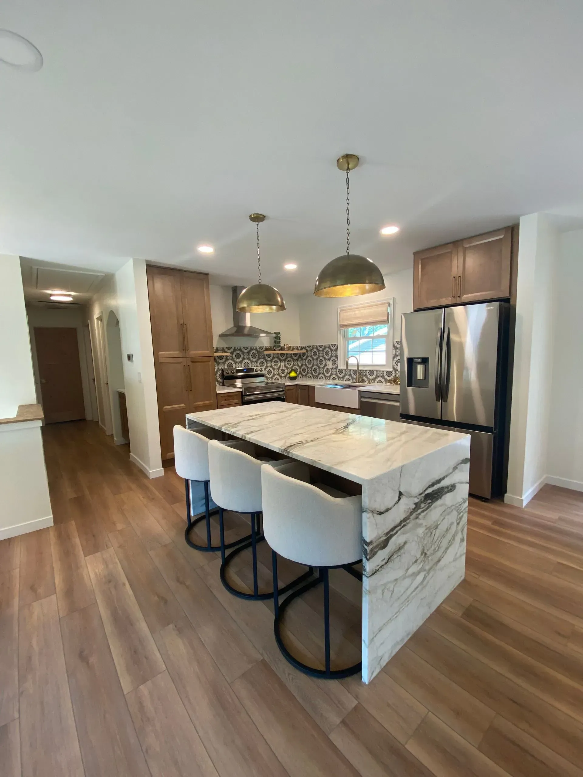 Modern kitchen with island, marble countertop, pendant lights, stainless steel appliances, and wood flooring.