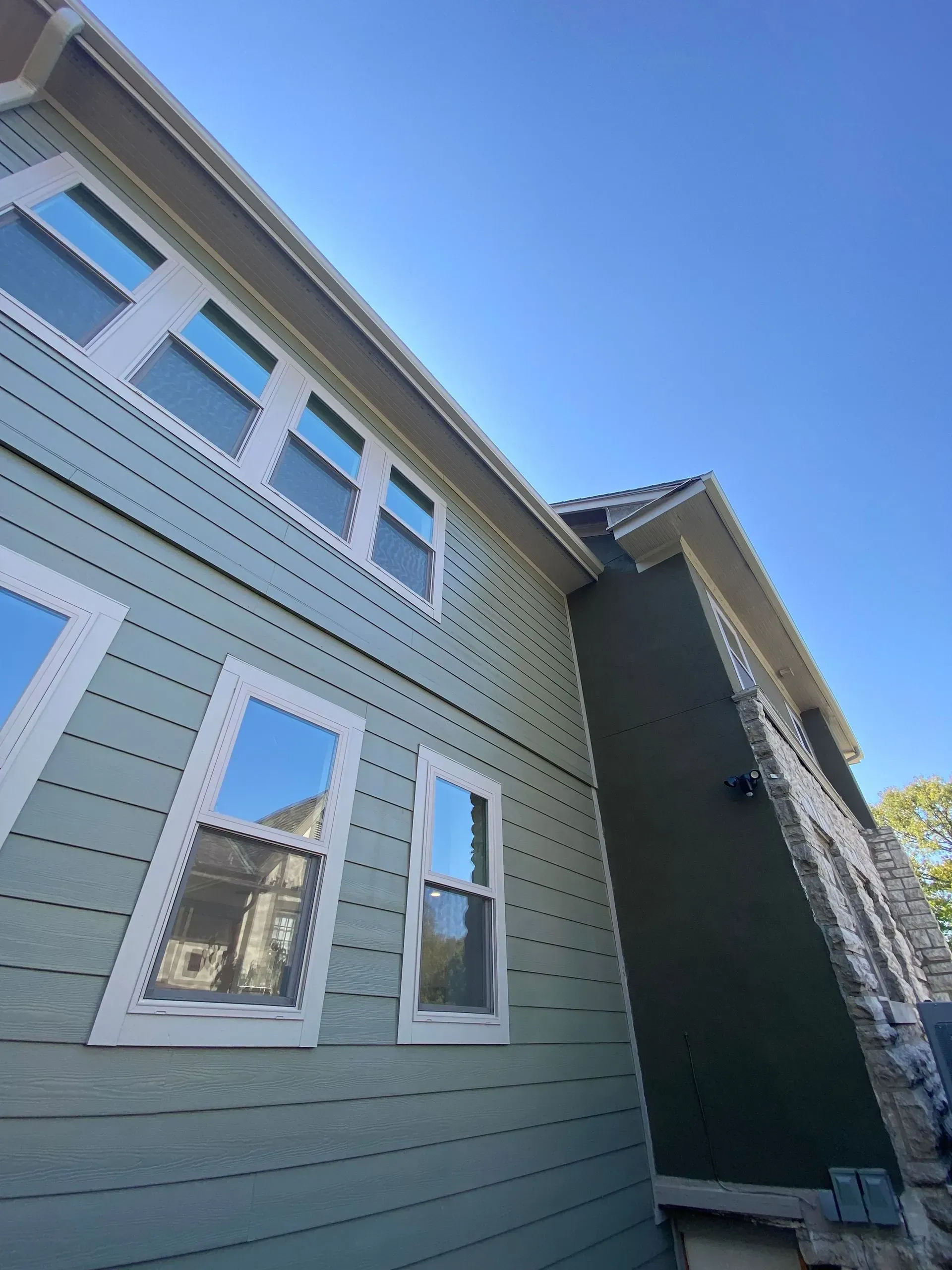 Blue-green siding on a house with white trim and a brown roof against a clear blue sky.