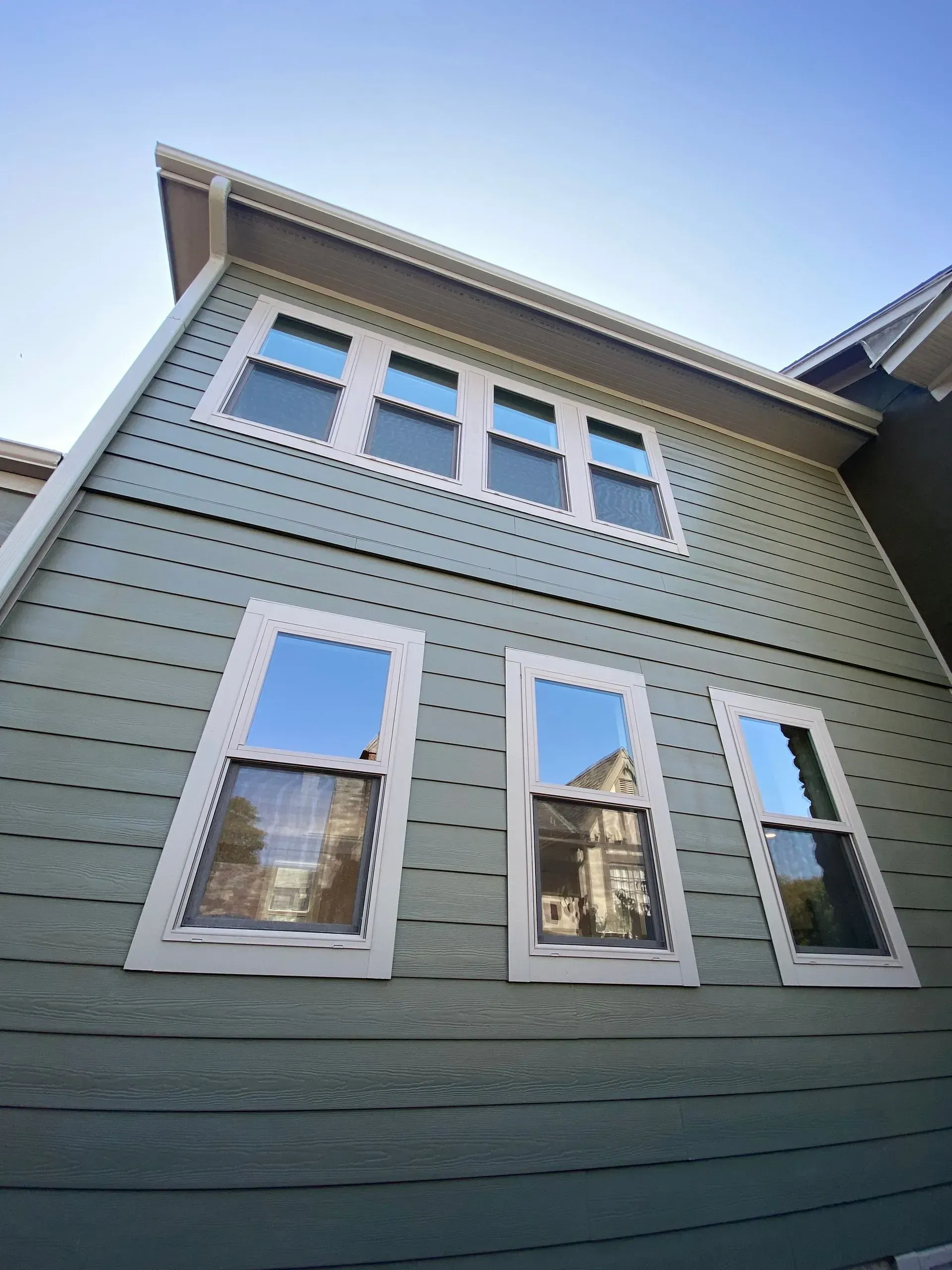 Green house exterior with white-framed windows reflecting the sky.