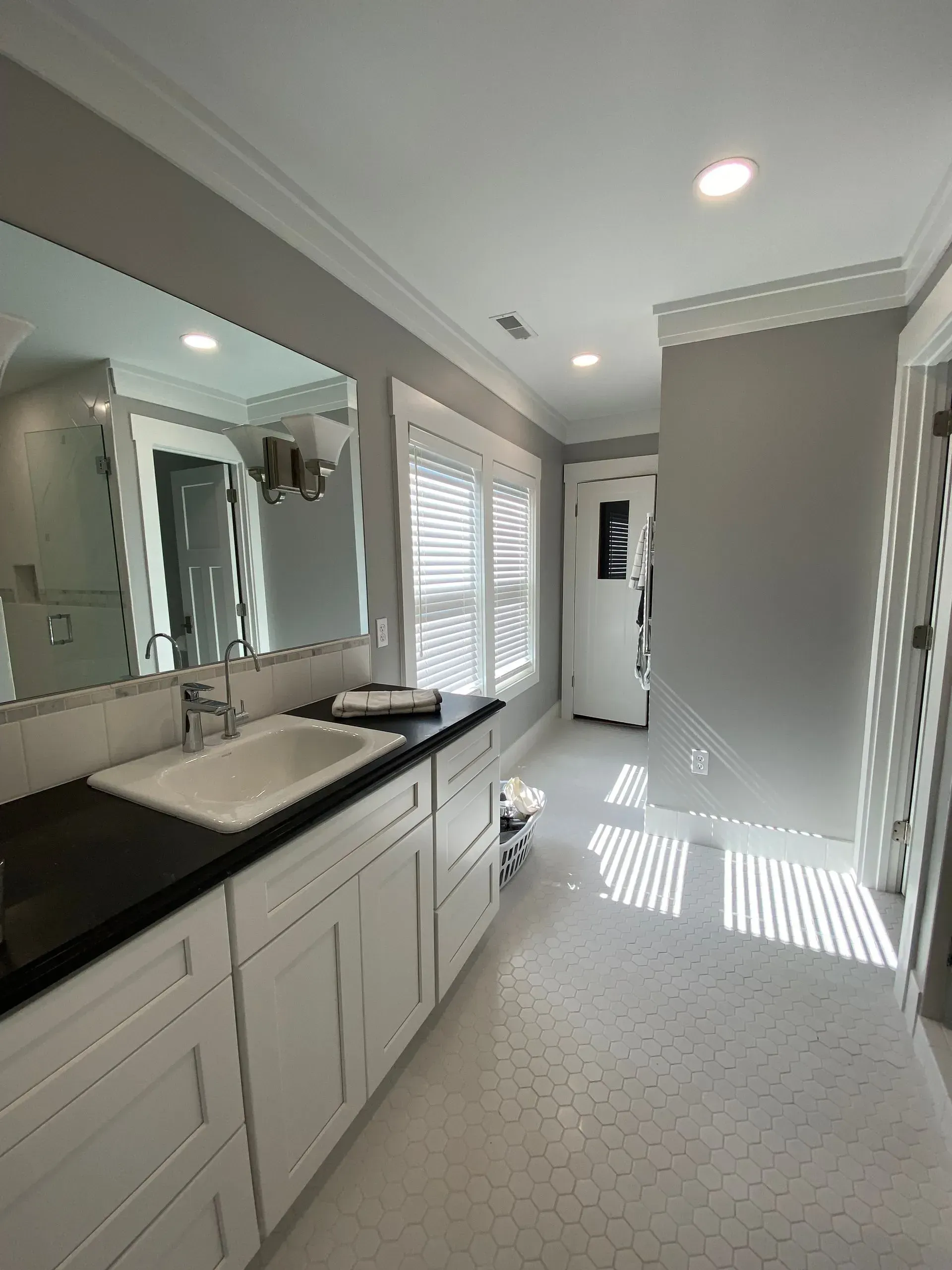 Bathroom with white cabinets, gray walls, and natural light from window with blinds.