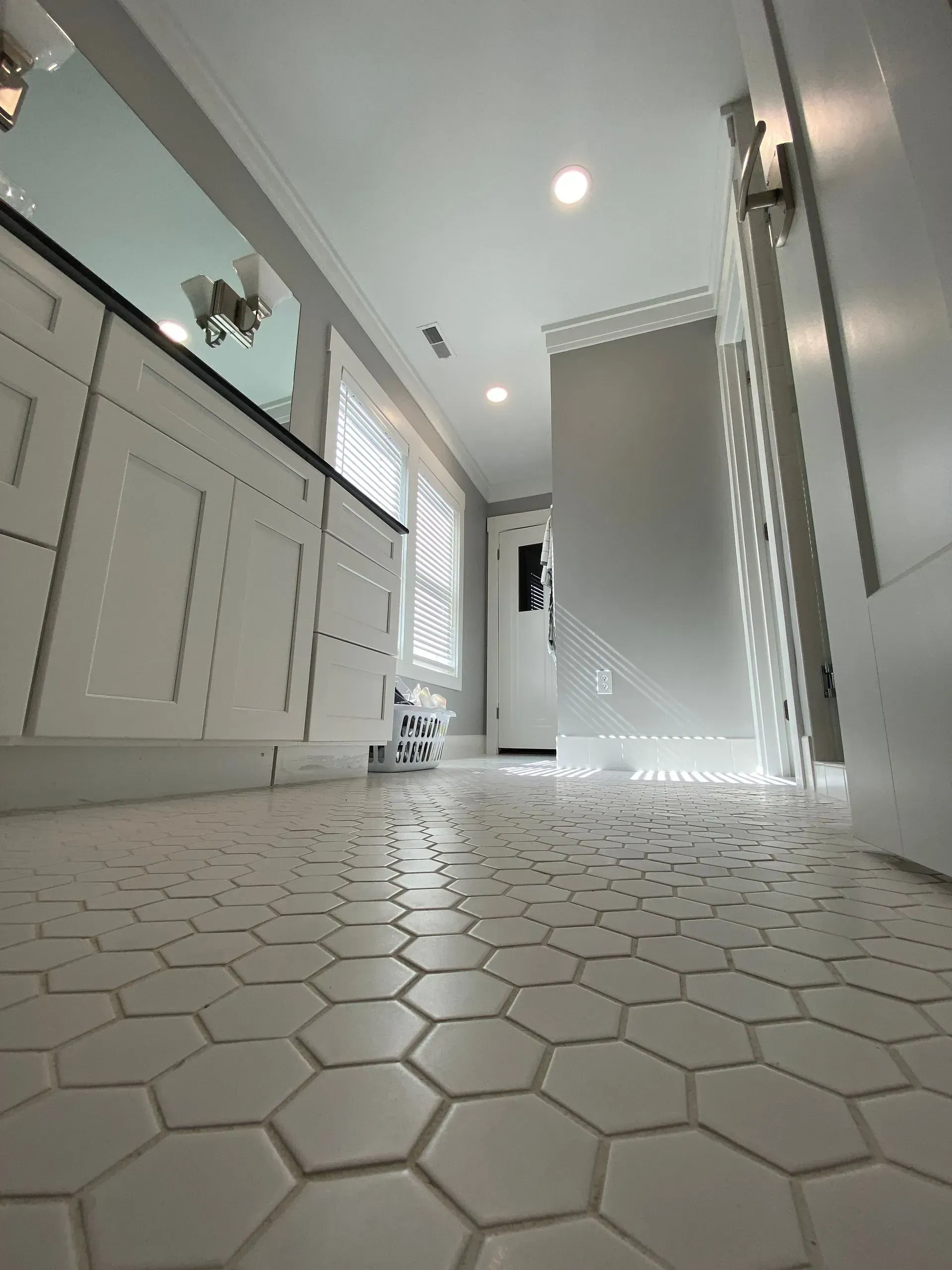 White hexagon tile floor in a bright bathroom, cabinets to the left, doorway at the end.