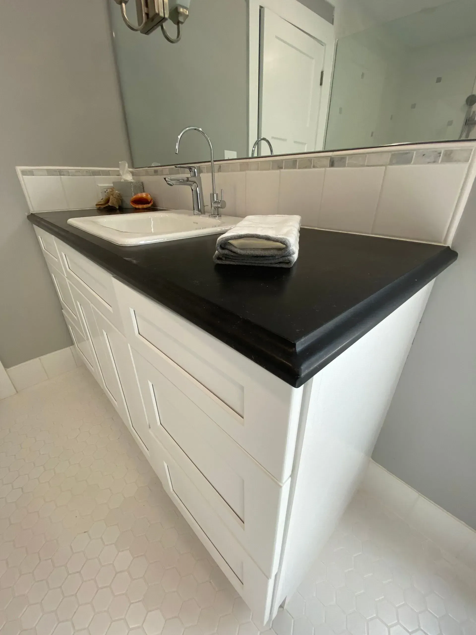 White bathroom vanity with black countertop and white hexagonal floor tiles.