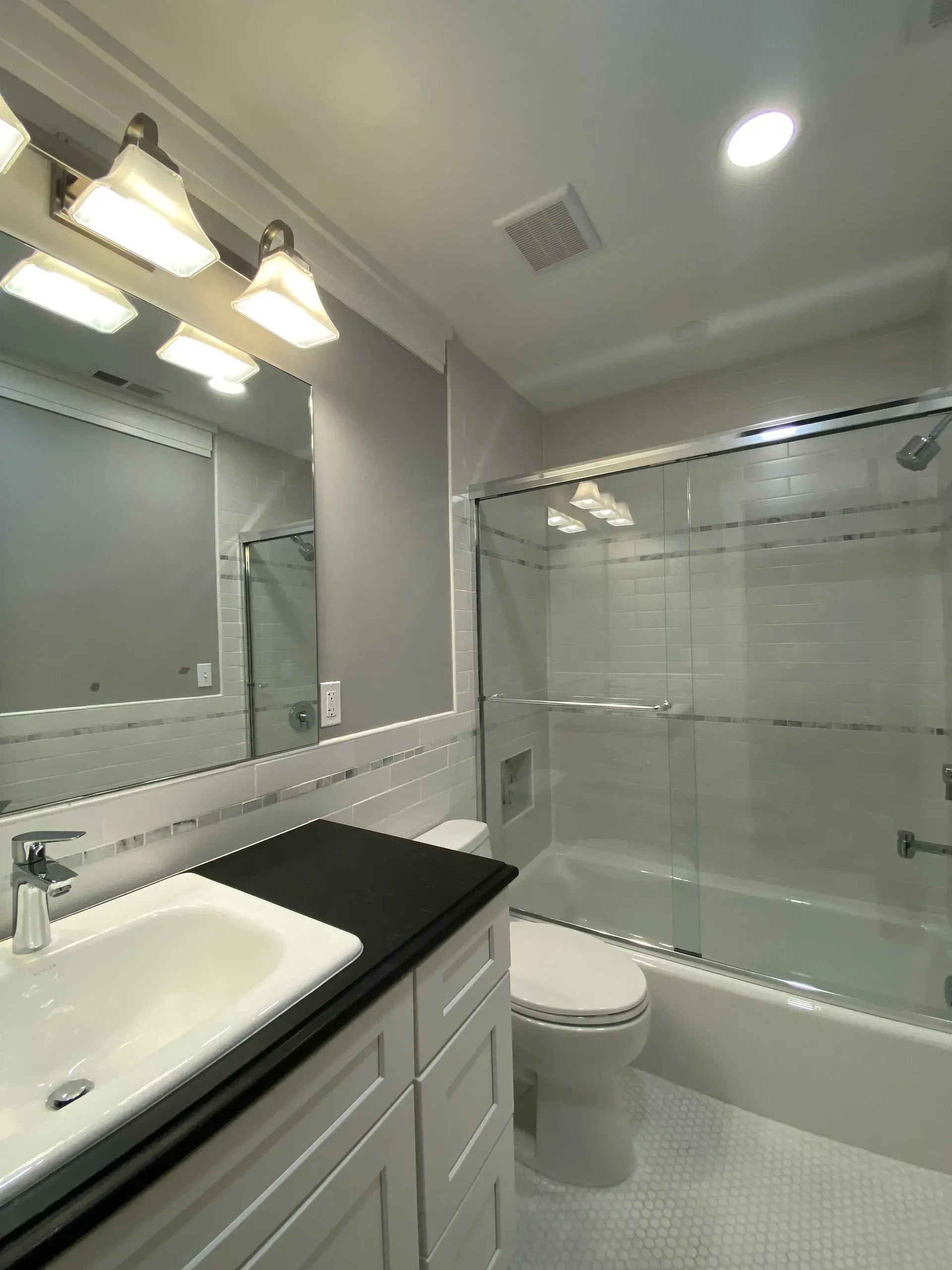 Modern bathroom with white vanity, toilet, glass shower, and gray walls.