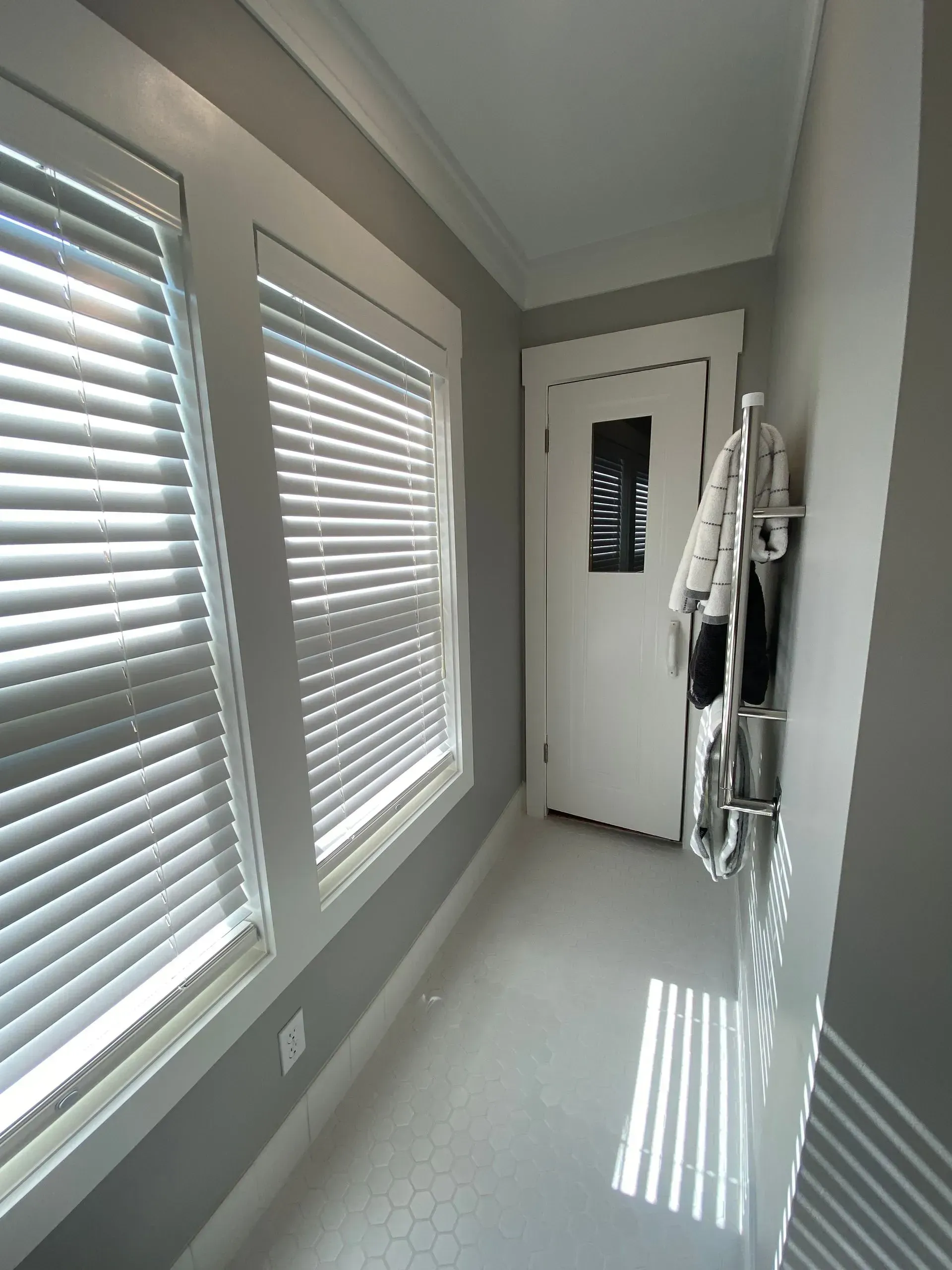 Narrow hallway with blinds, door, and coat rack; light streams in.