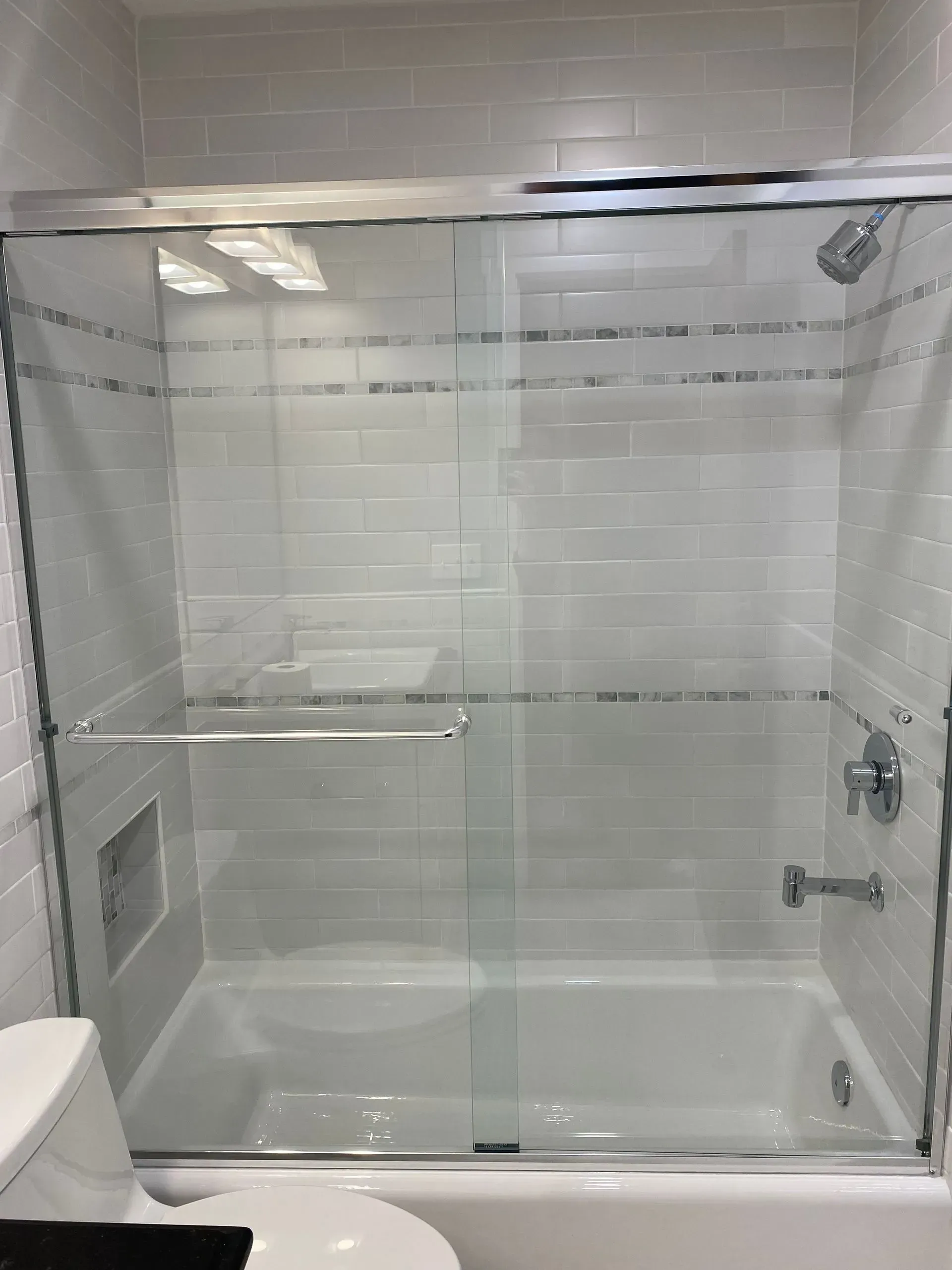 A white-tiled bathroom with a glass sliding shower door. A toilet is visible in the bottom left corner.