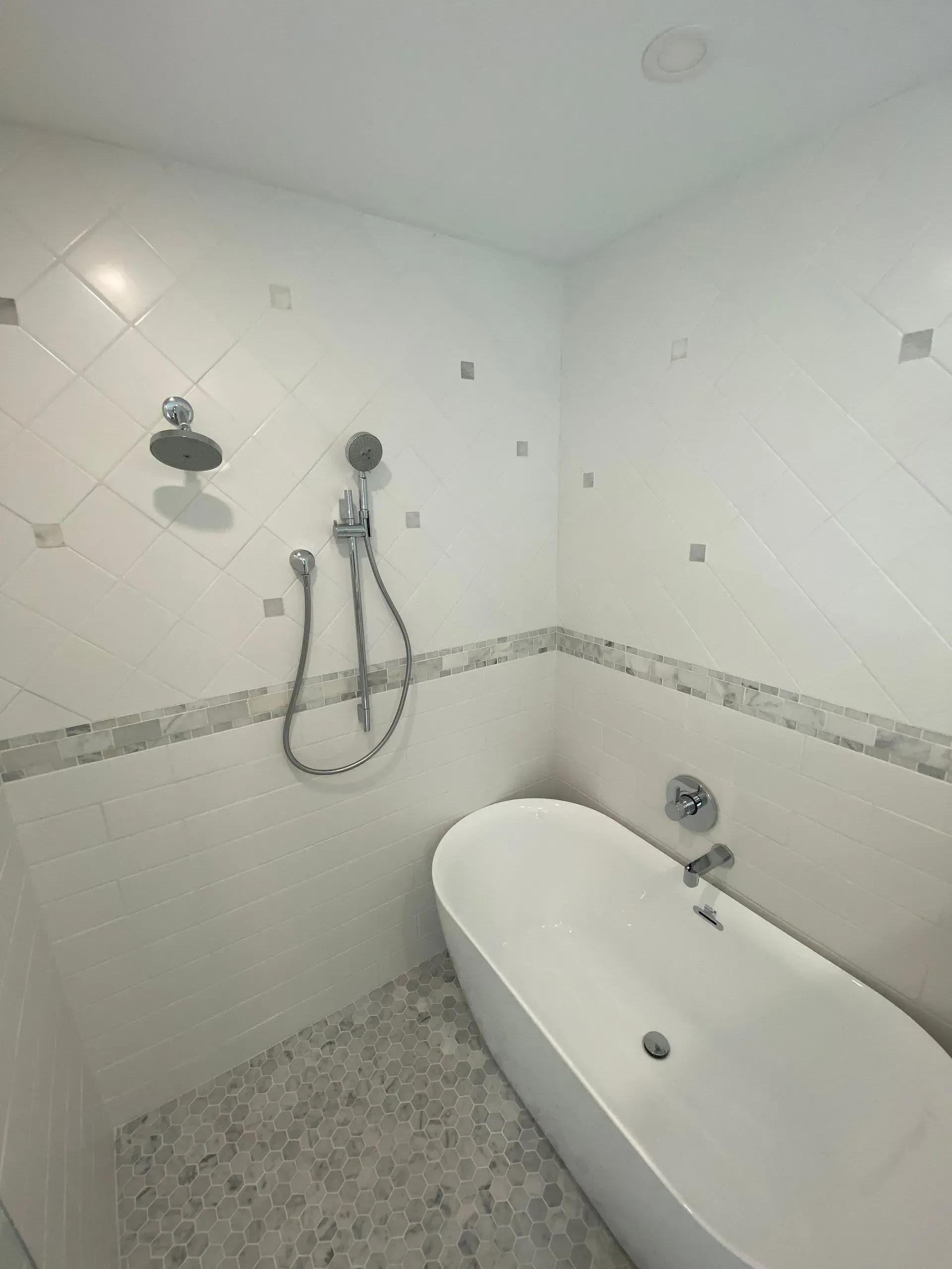 White-tiled shower/bath combo with a freestanding tub. Features a rain showerhead, handheld shower, and mosaic tile floor.