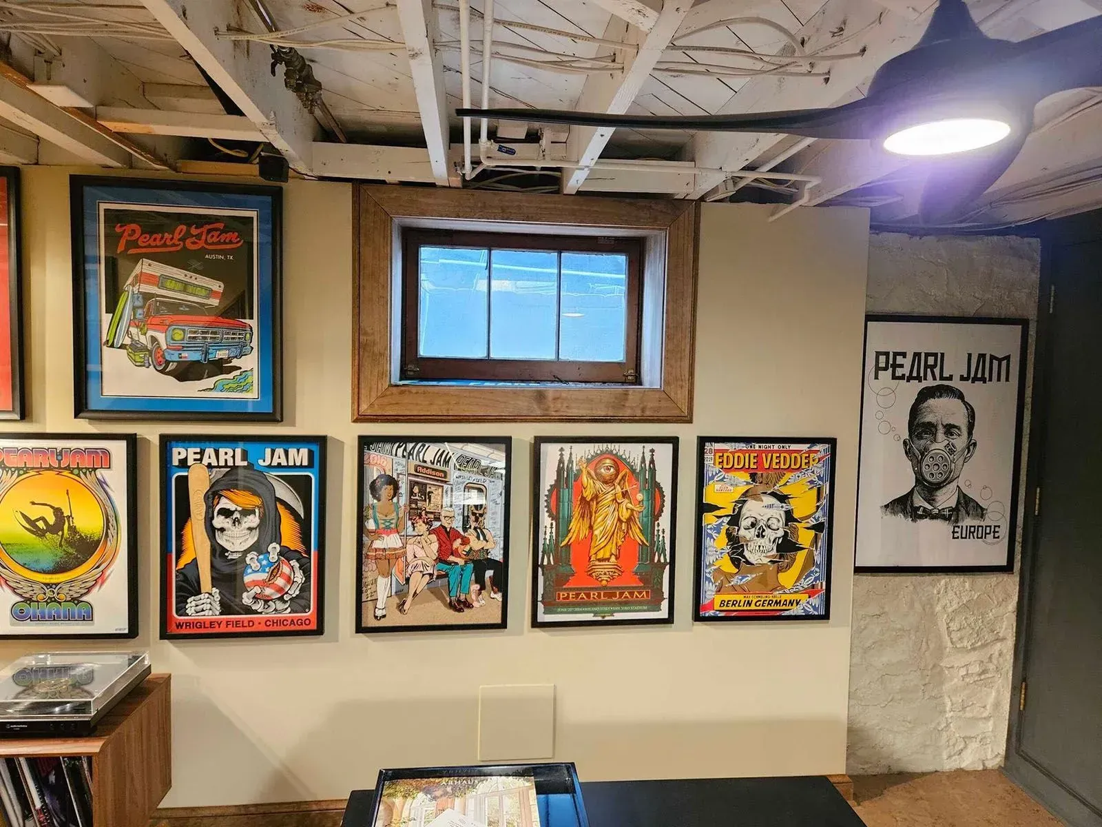 Collection of framed Pearl Jam concert posters and memorabilia on a basement wall with a small window.