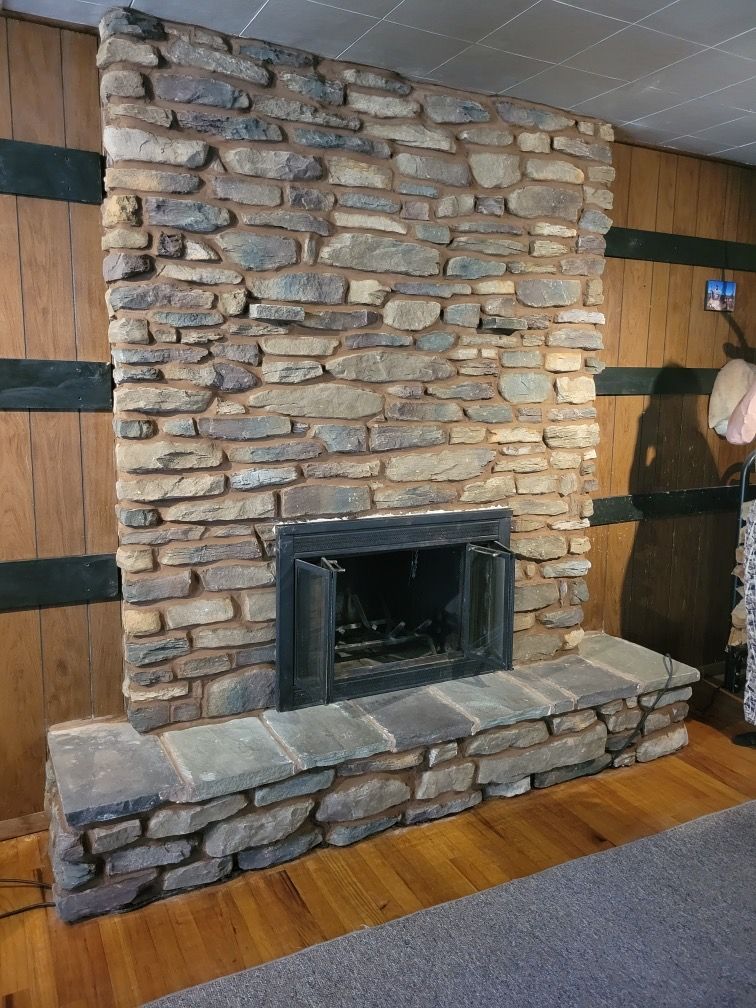 A large stone fireplace in a living room with wood paneling.