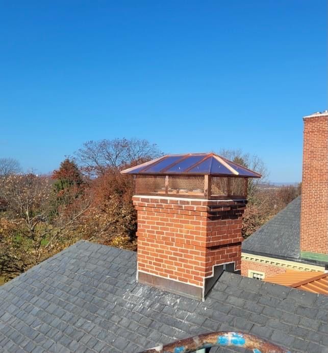 A brick chimney on top of a roof with a blue sky in the background