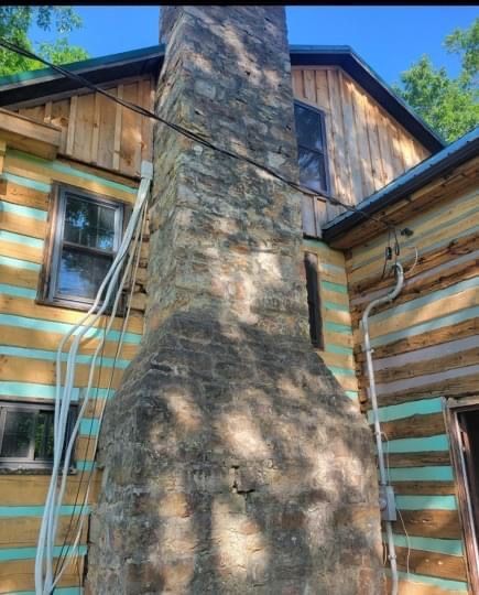 A large stone chimney on top of a building with a green roof.