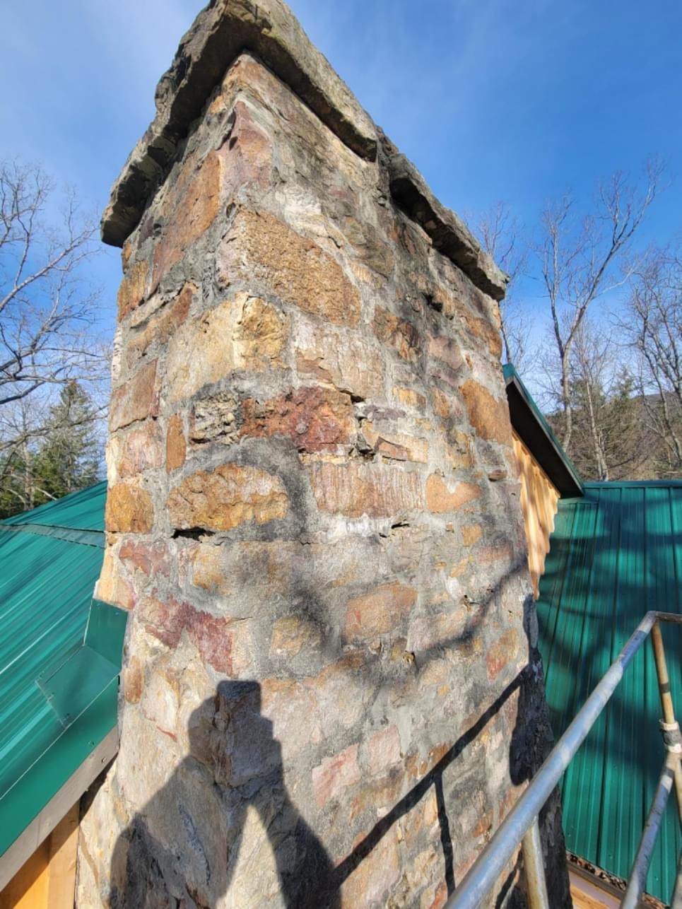 A stone chimney on top of a house with a green roof.