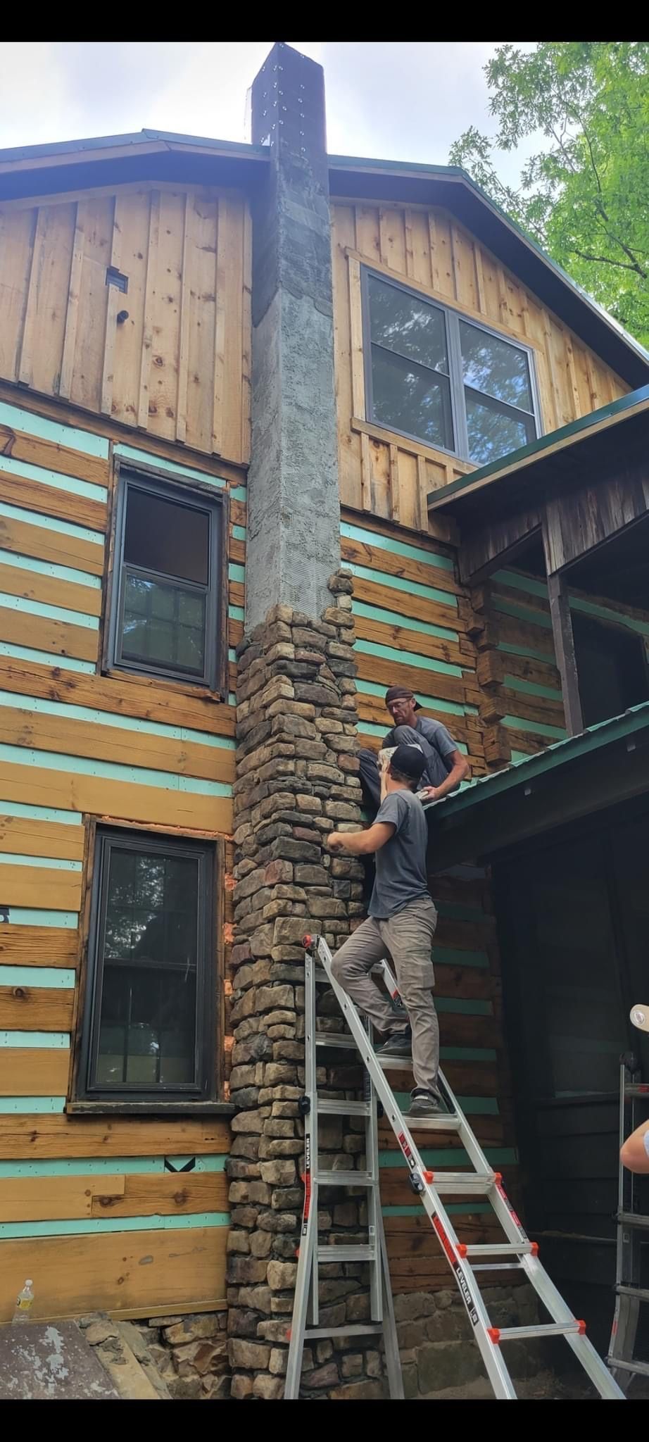 A man is standing on a ladder in front of a log cabin.