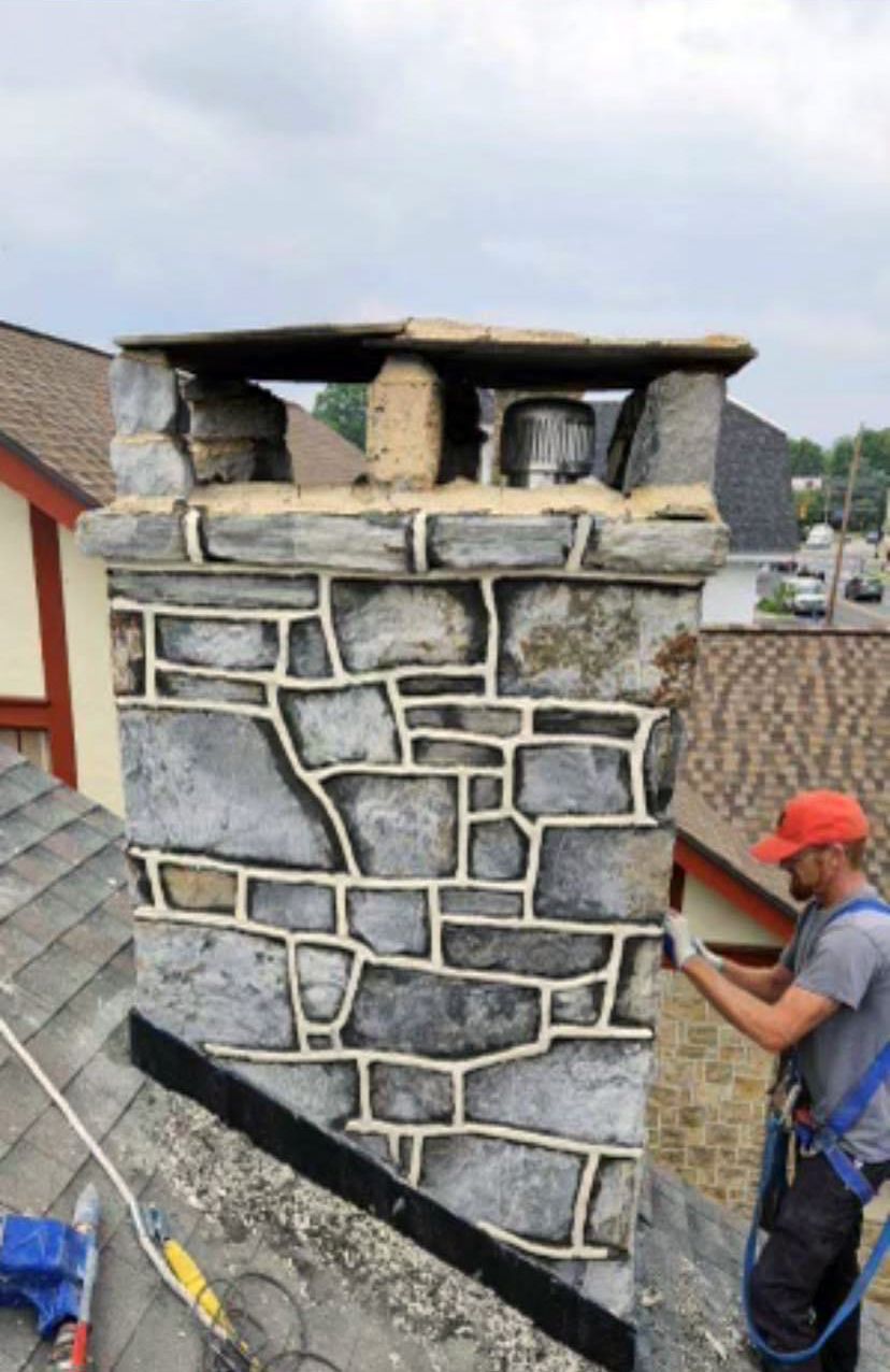A man is working on a stone chimney on top of a roof.