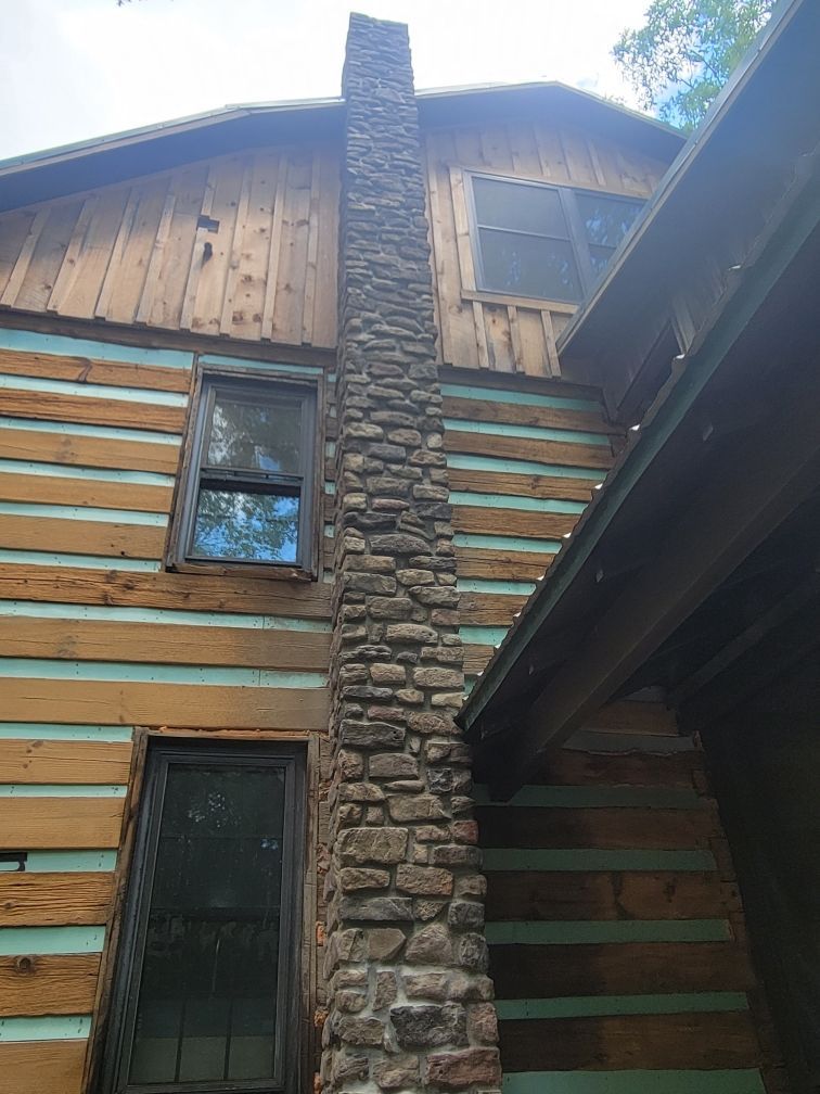 A log cabin with a stone chimney on the side of it.