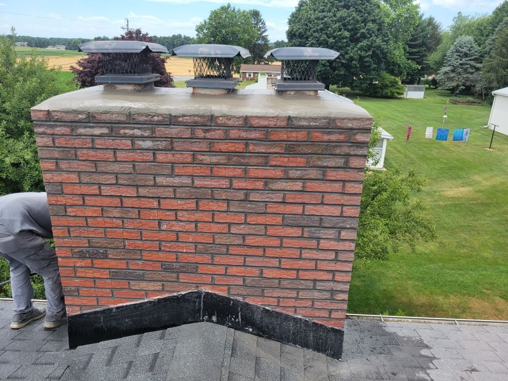 A man is working on a brick chimney on top of a roof.